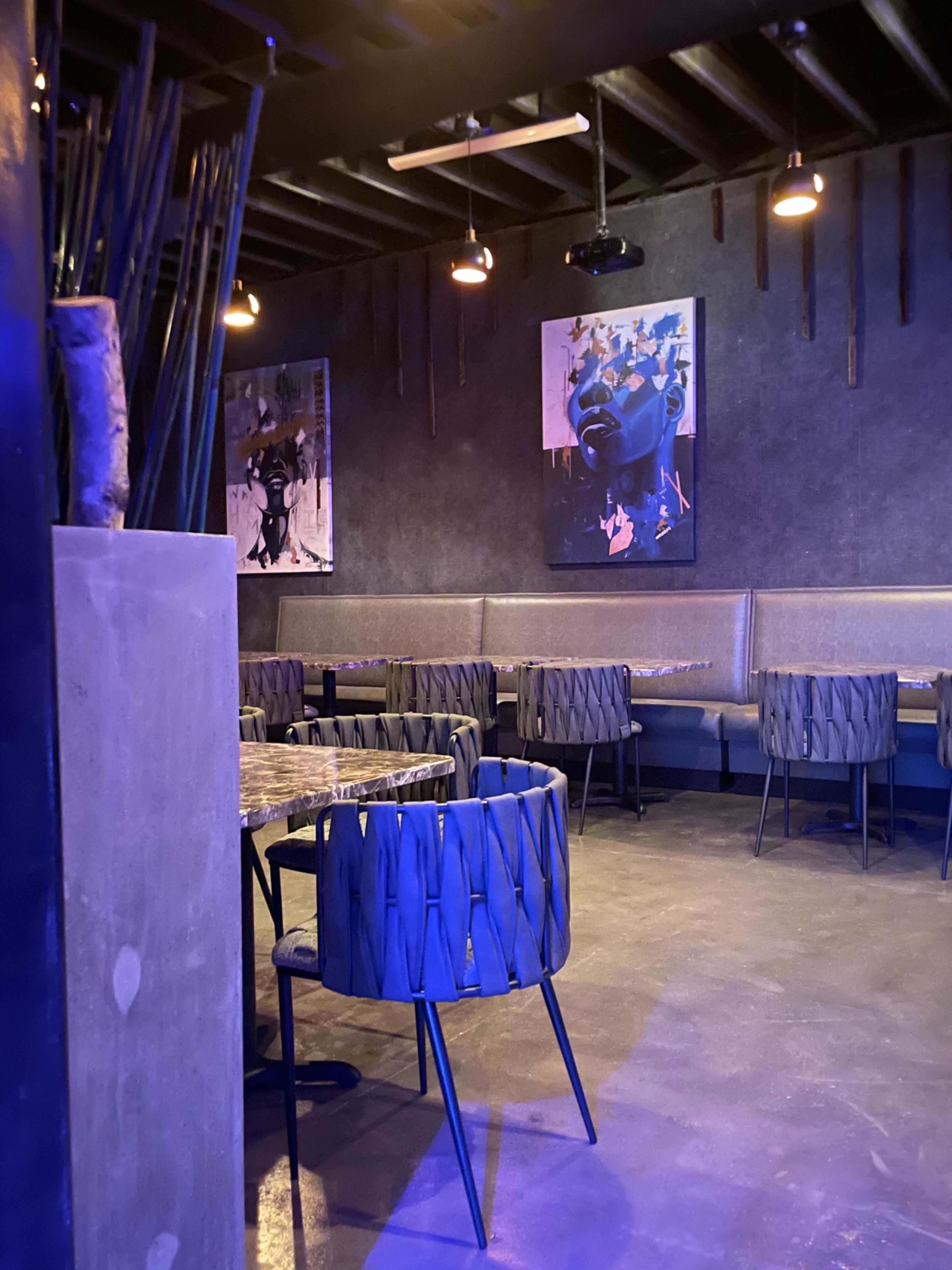 The image shows an interior of a dimly lit restaurant featuring modern art on the walls, angular seating, and dark decor.