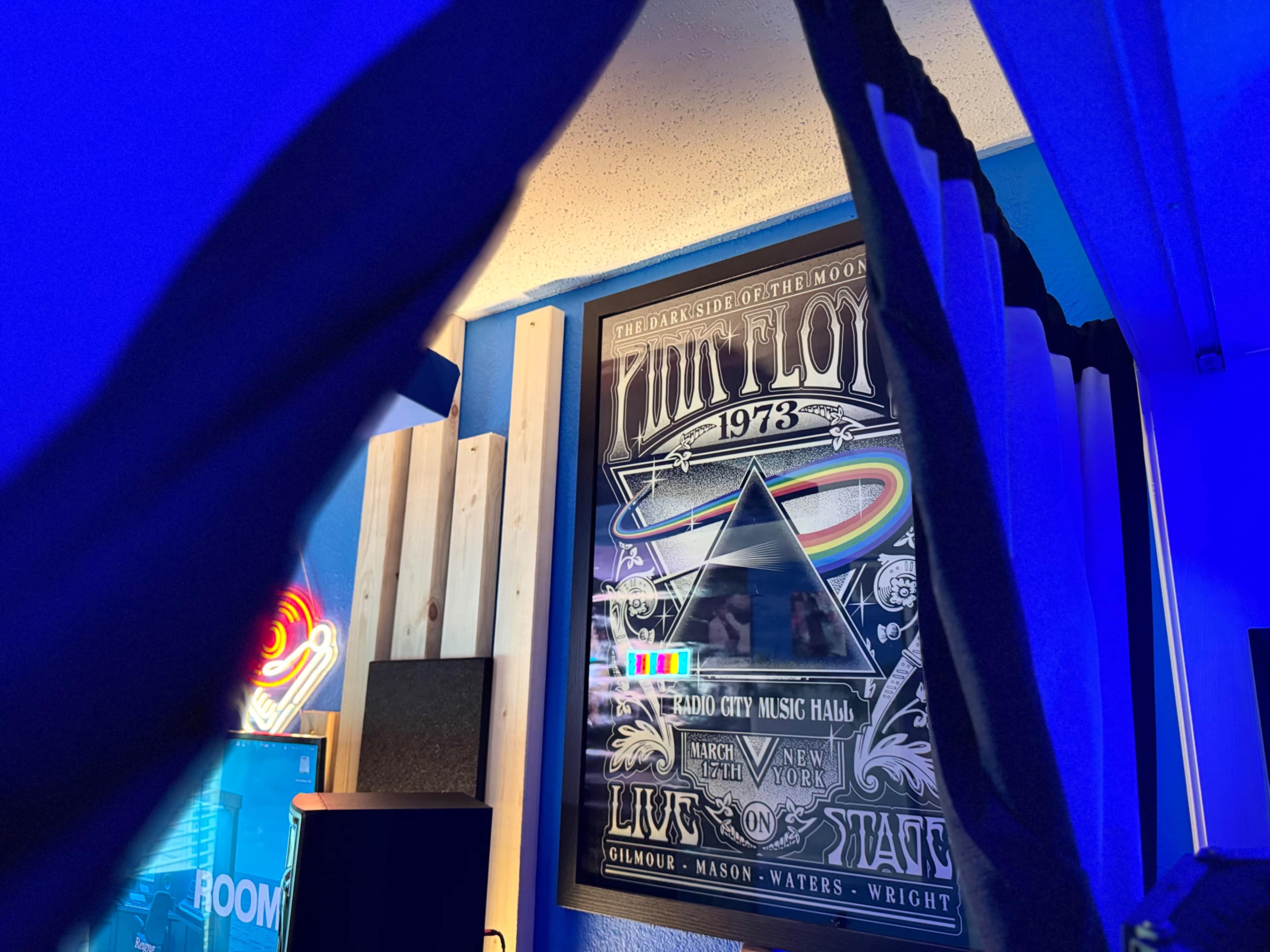 The image features a framed poster of Pink Floyd's "The Dark Side of the Moon," displayed in a room with blue lighting and various furnishings.