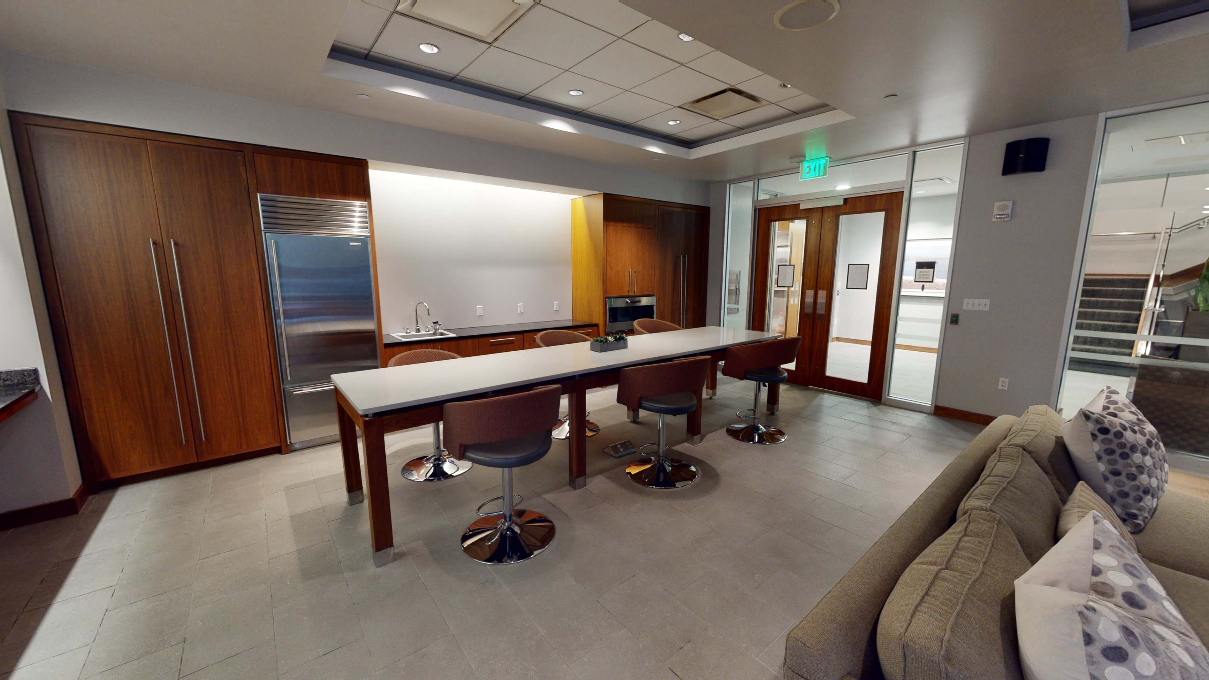 The image shows a modern kitchen with wooden cabinetry, a large island with three stools, and stainless steel appliances.