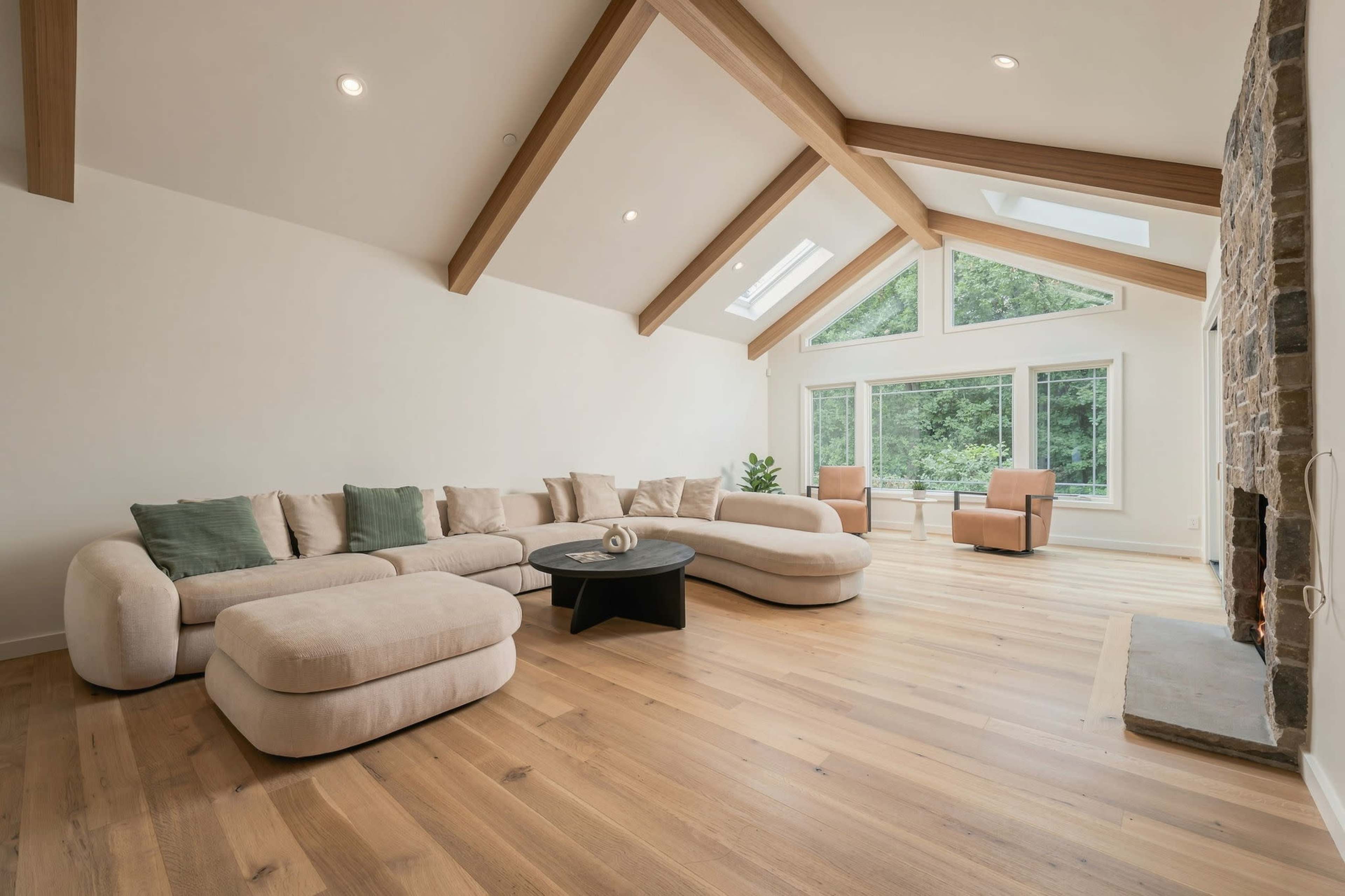 The image depicts a spacious living room with a large, curved sectional sofa, a black coffee table, and large windows allowing natural light to fill the space.