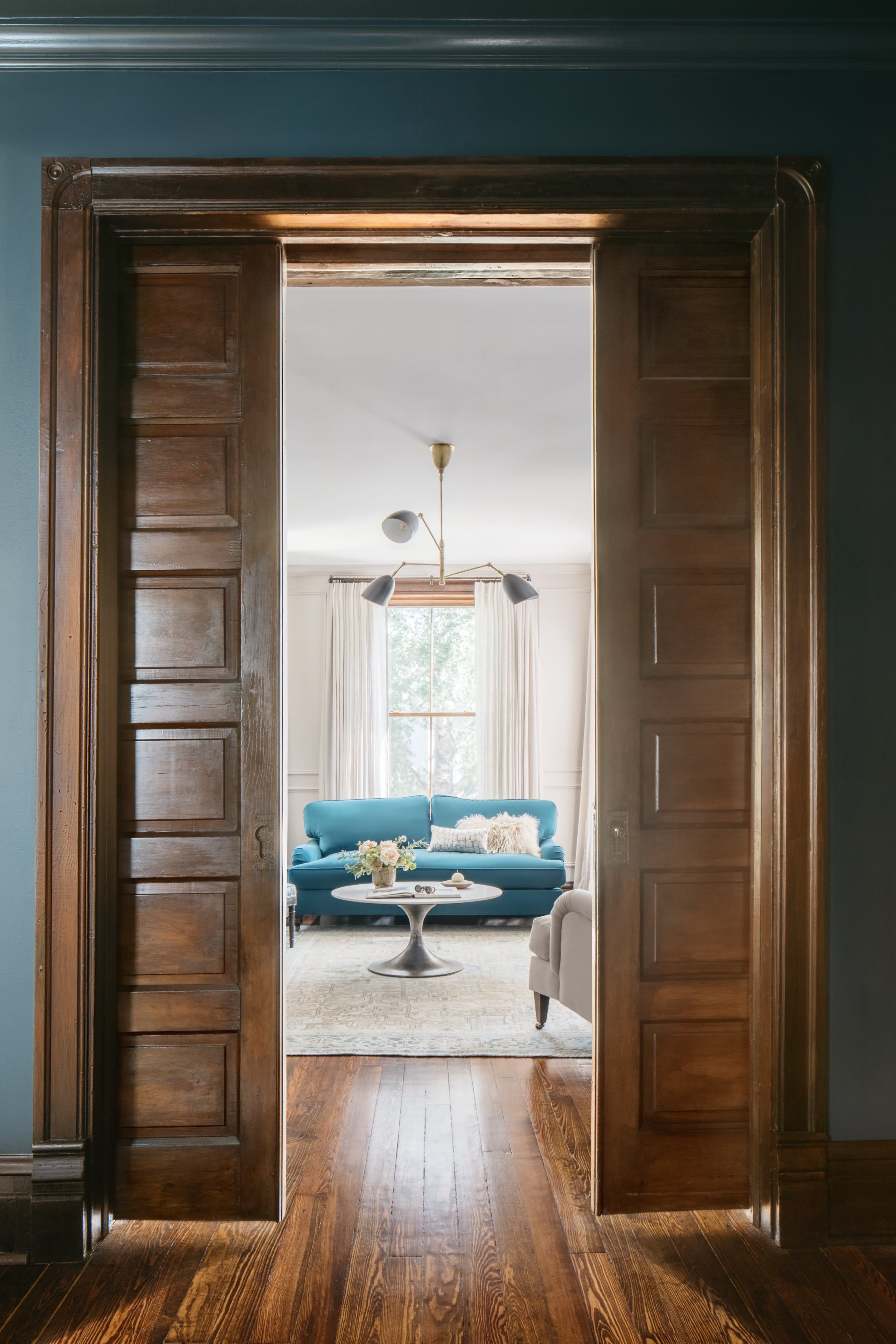 A doorway with wooden double doors leading into a bright living room featuring a blue sofa and a coffee table.