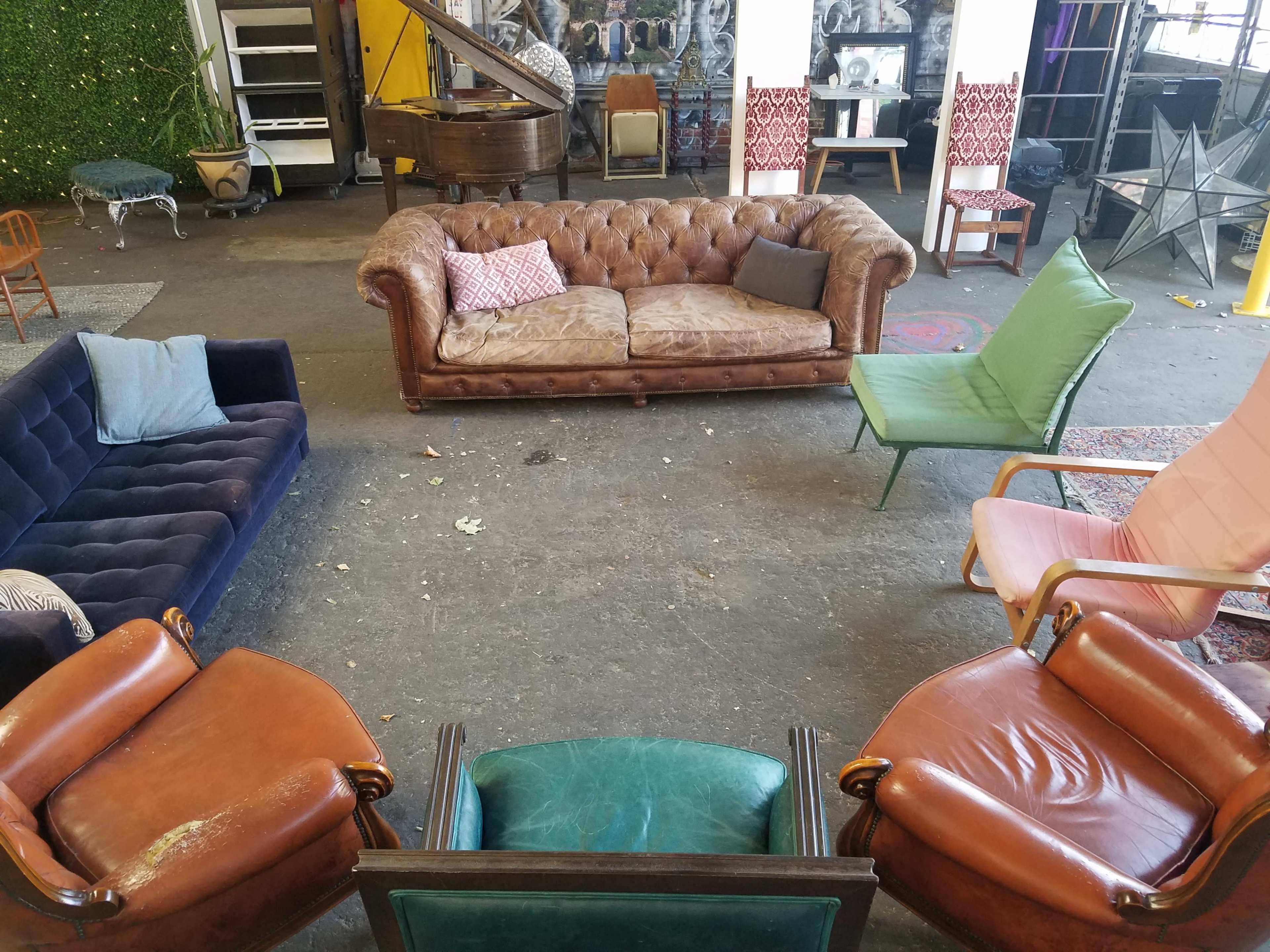 The image shows a variety of vintage seating options arranged in a spacious, industrial-style room with exposed brick walls and a mix of decorative elements.