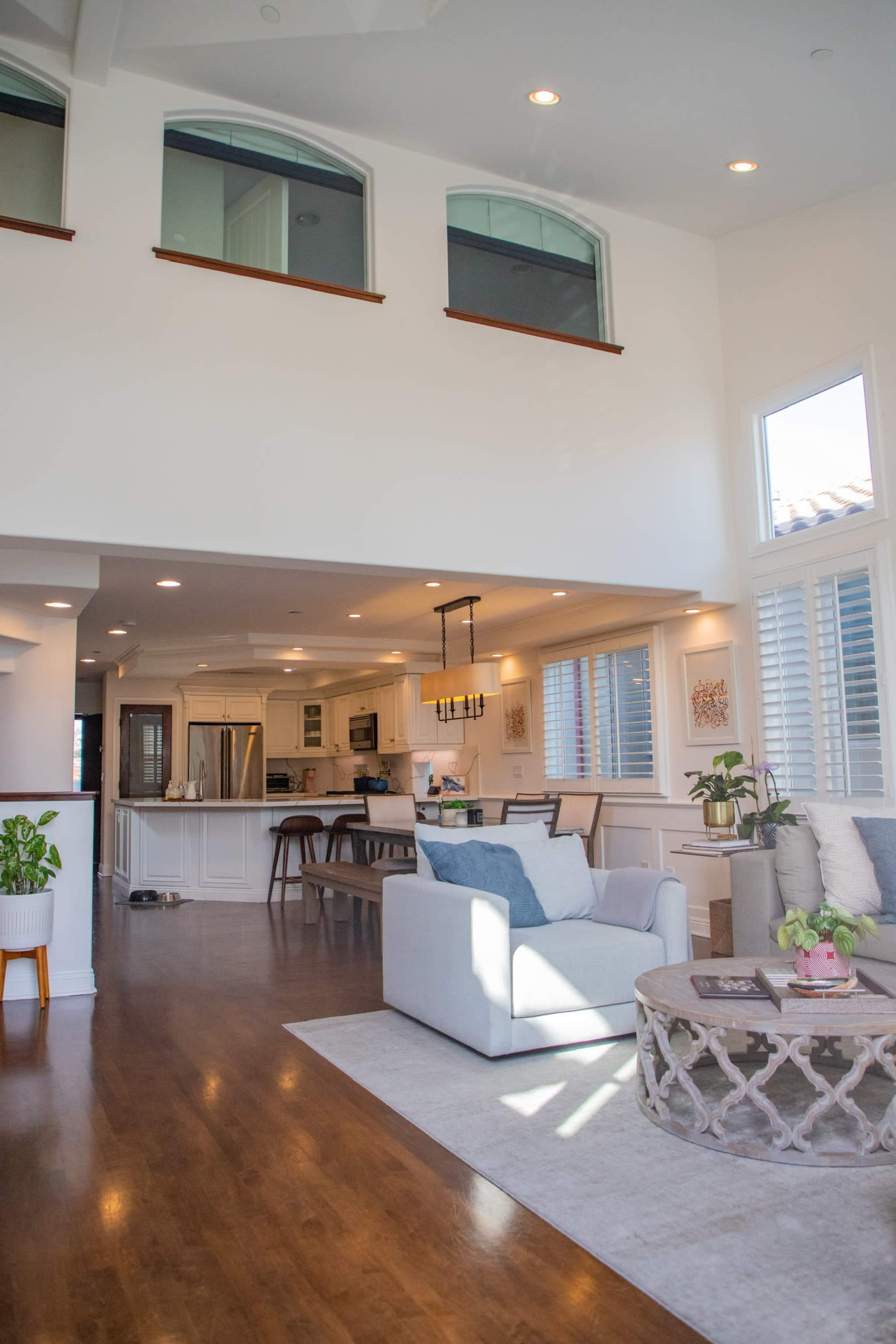 The image shows a well-lit open-concept living space with a seating area, dining area, and a kitchen in the background.