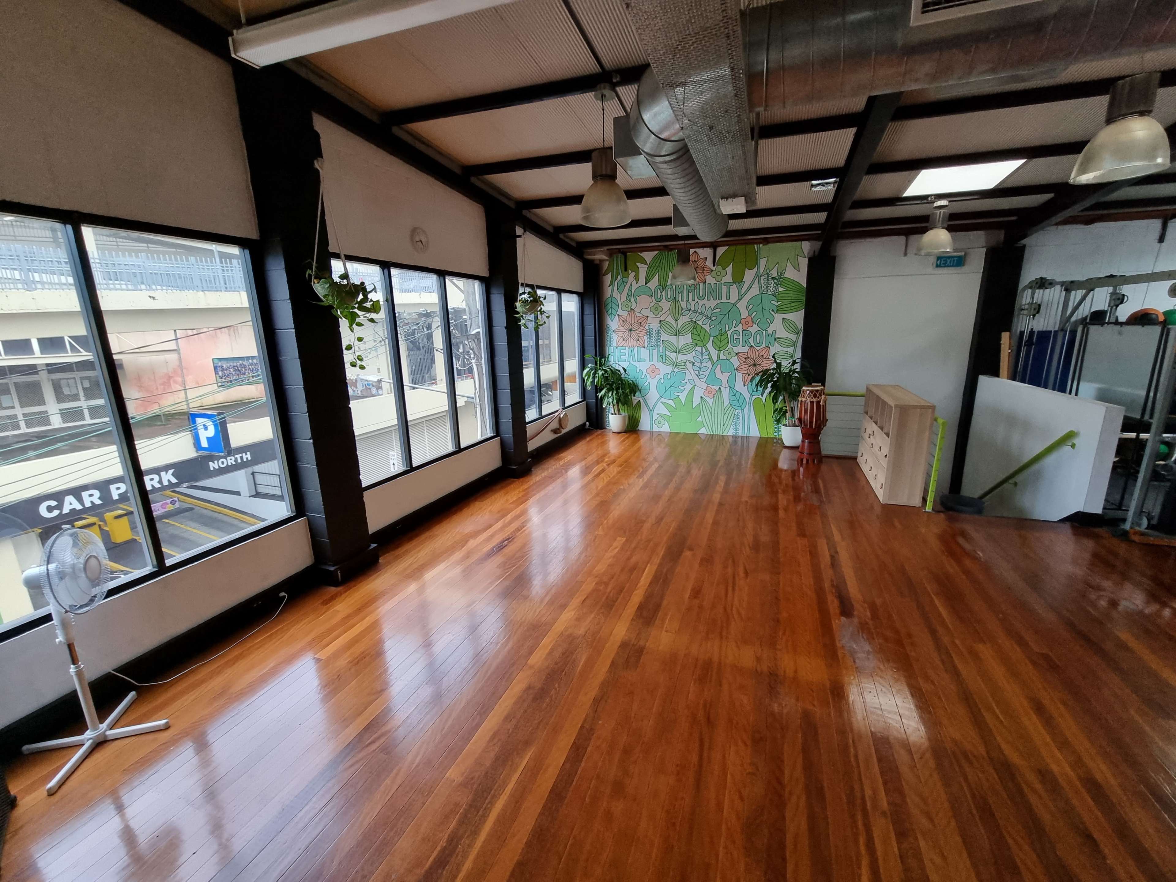 A spacious, brightly lit room with wooden floors, large windows, and a decorative wall featuring greenery.