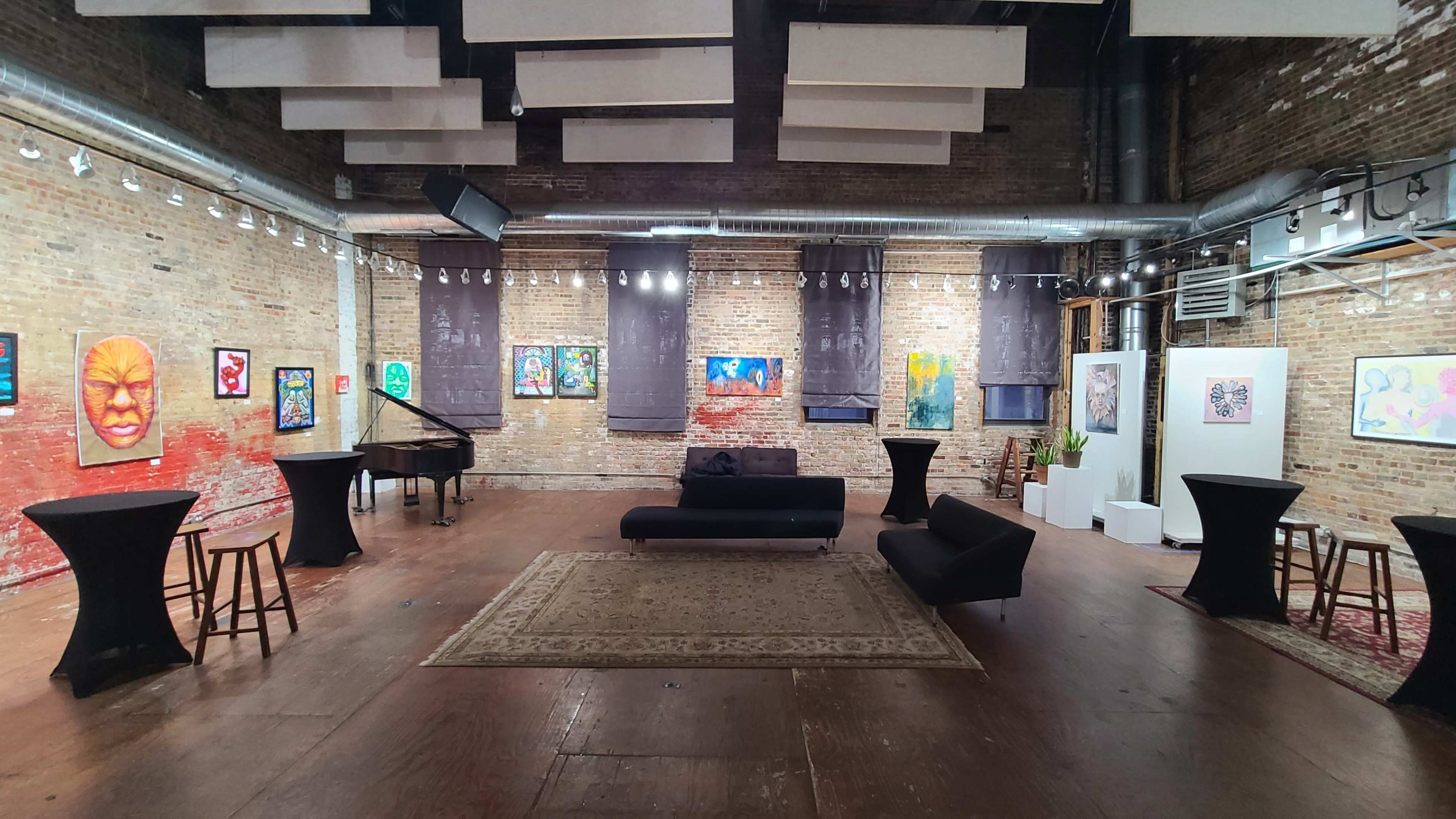 An art gallery featuring colorful paintings on the brick walls, with a piano and several lounge areas arranged around a central rug.