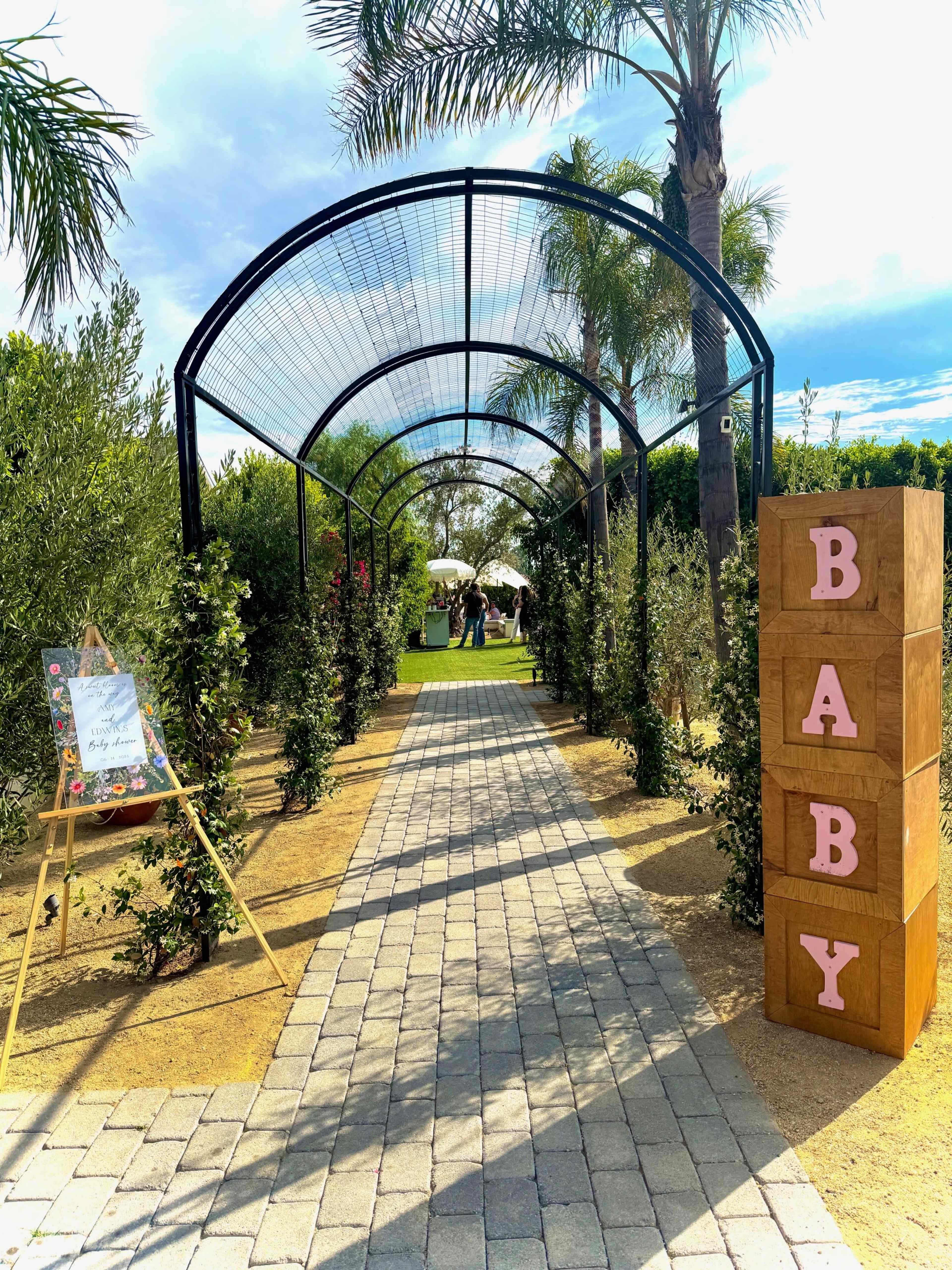 A path lined with greenery leads to a shaded archway, where wooden blocks spell out "BABY" on the side.