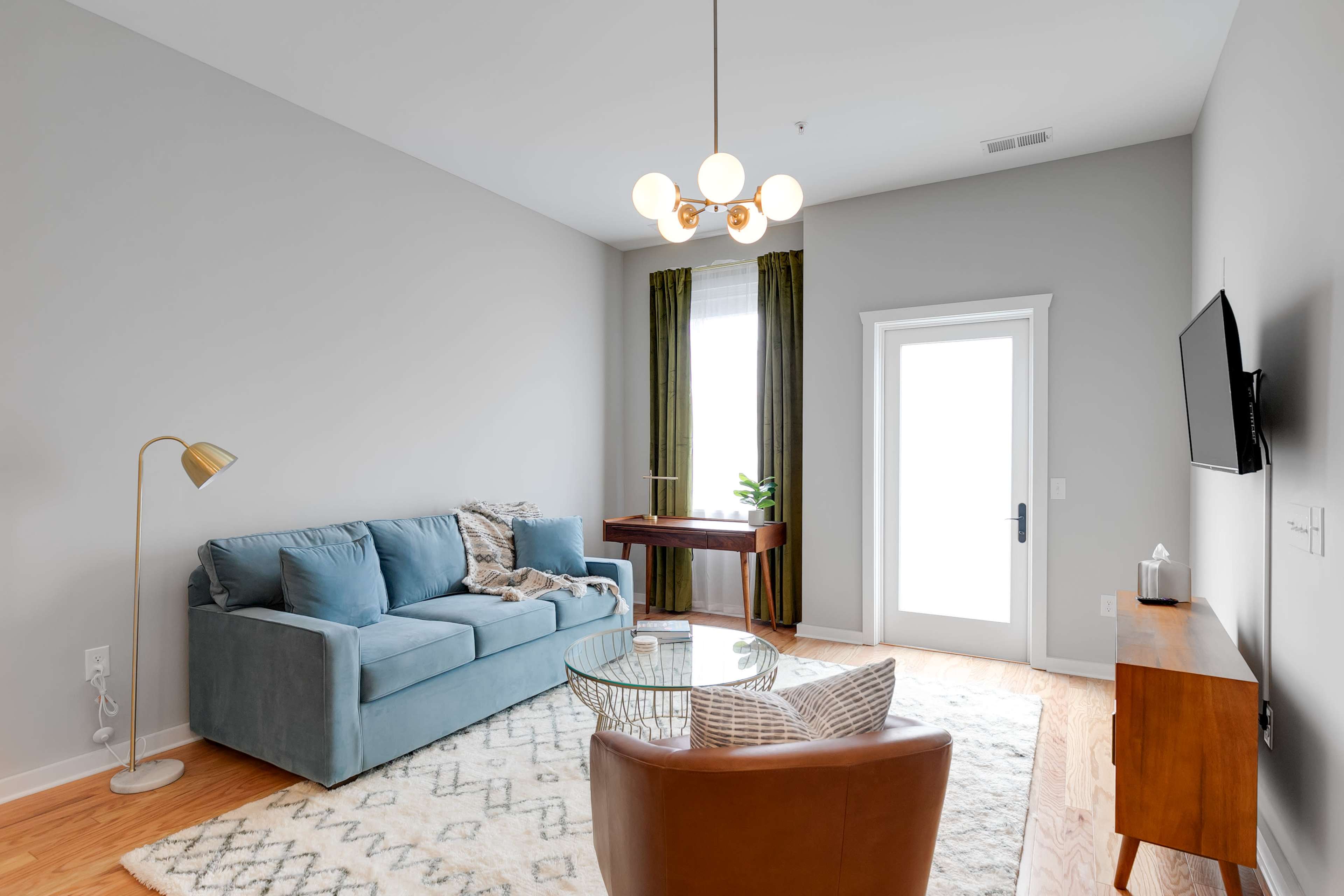 A modern living room featuring a blue sofa, a brown chair, a round coffee table, and a large window with green curtains.