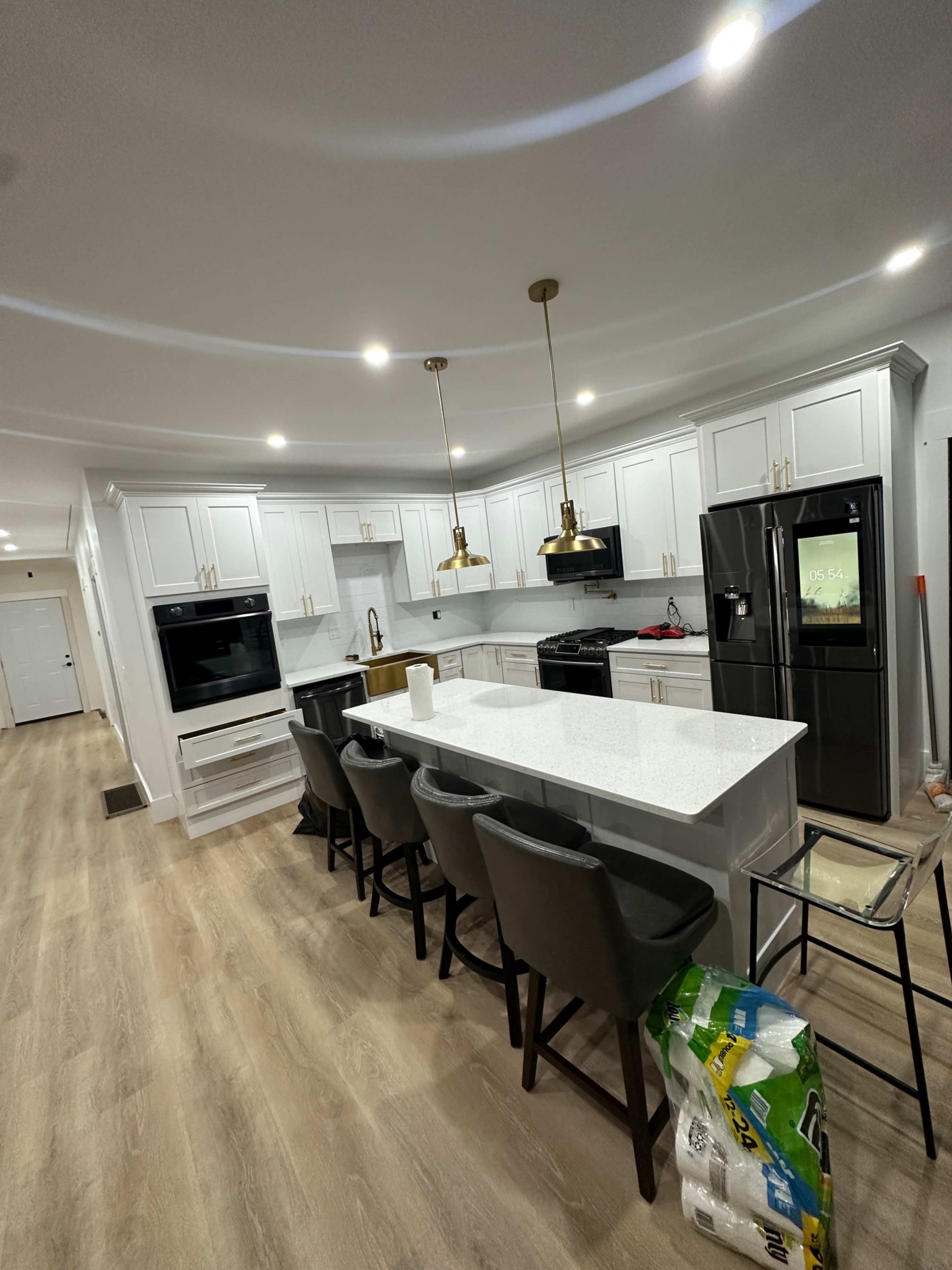 A modern kitchen features white cabinets, a central island with seating, and black appliances against a light wood floor.
