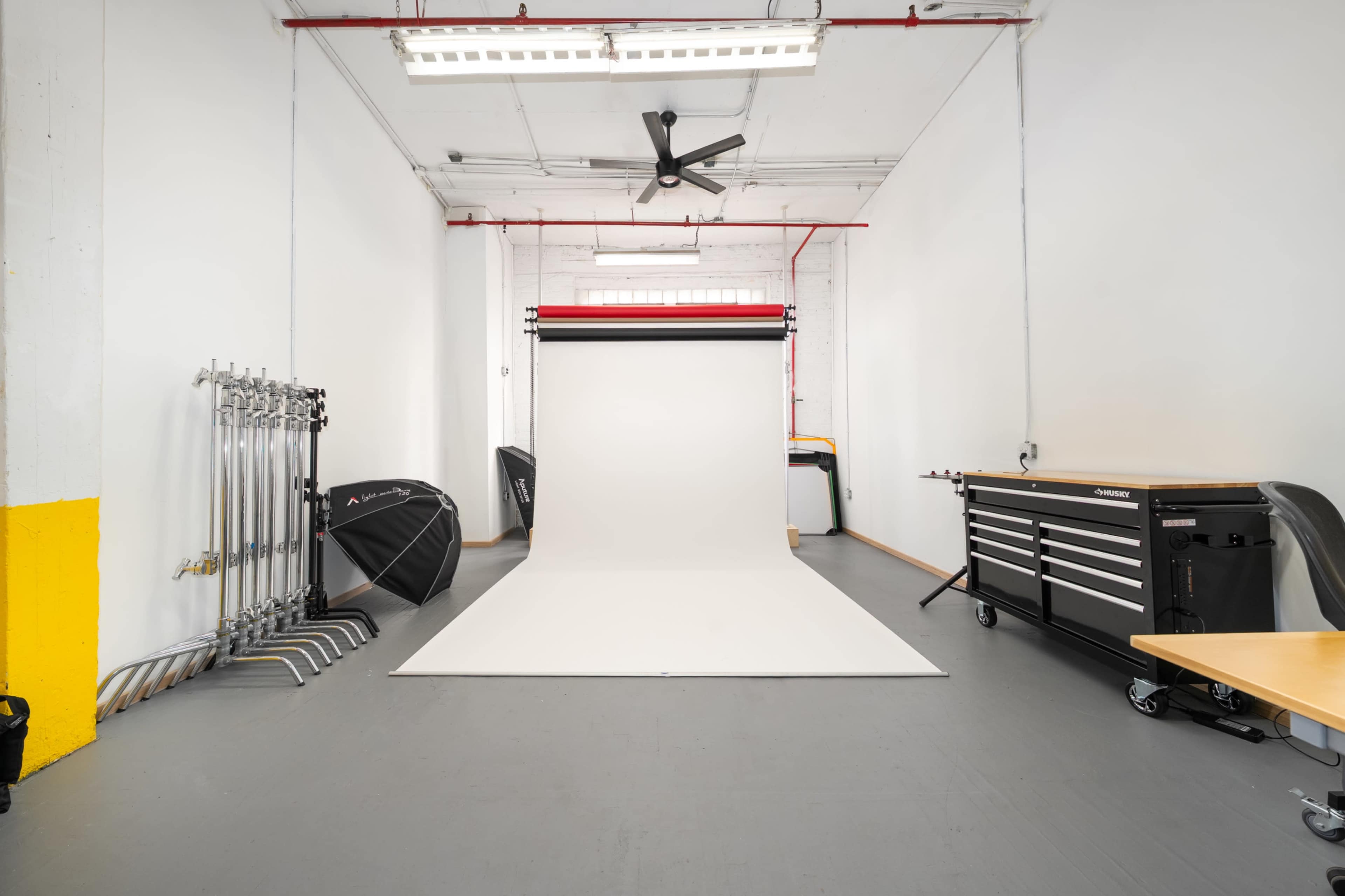 The image shows a photography studio with a seamless white backdrop, lighting equipment, and a metal tool chest along one wall.