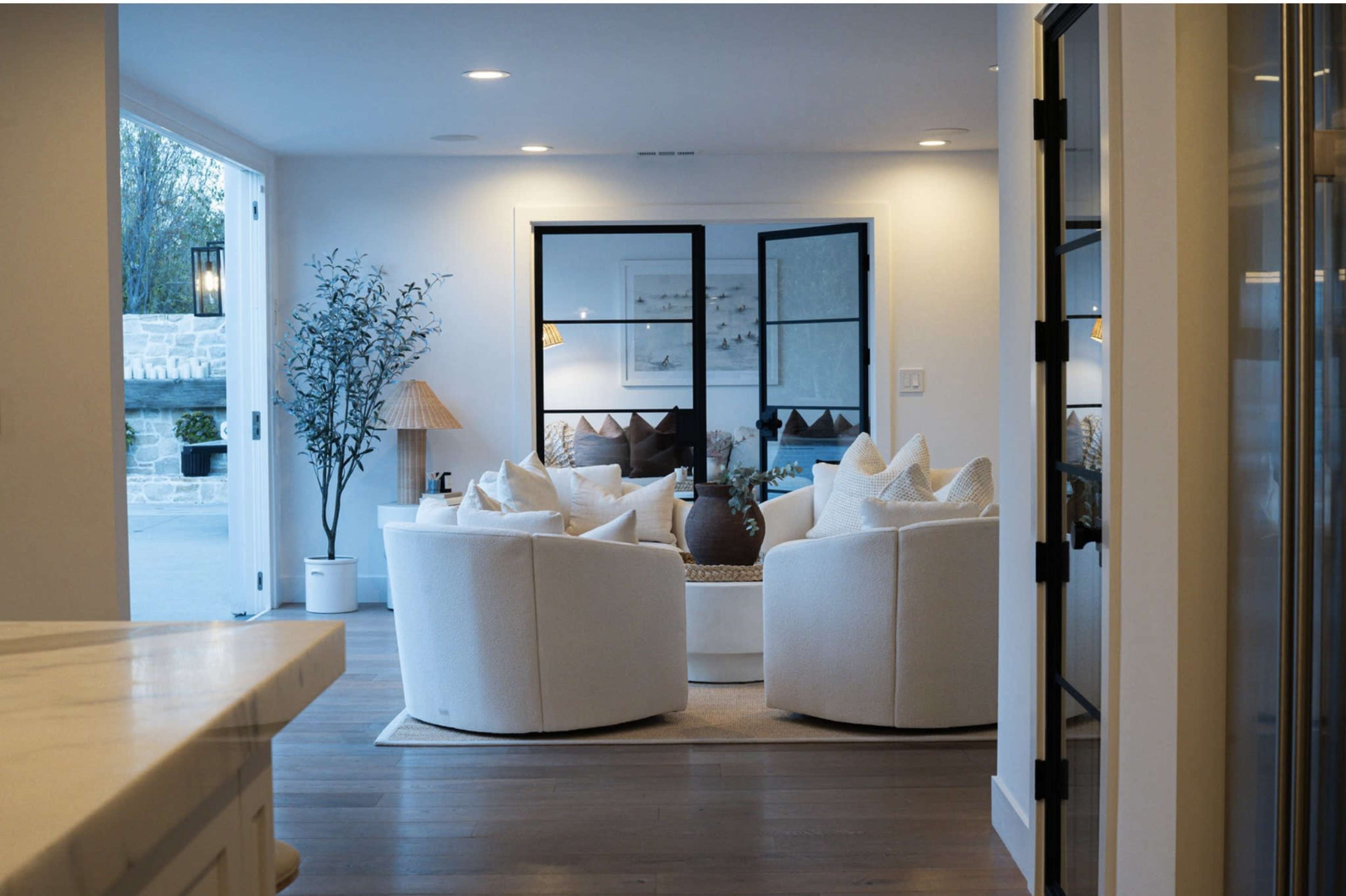 The image shows a modern living room with two round armchairs, a coffee table, and large windows that open to an outdoor area.