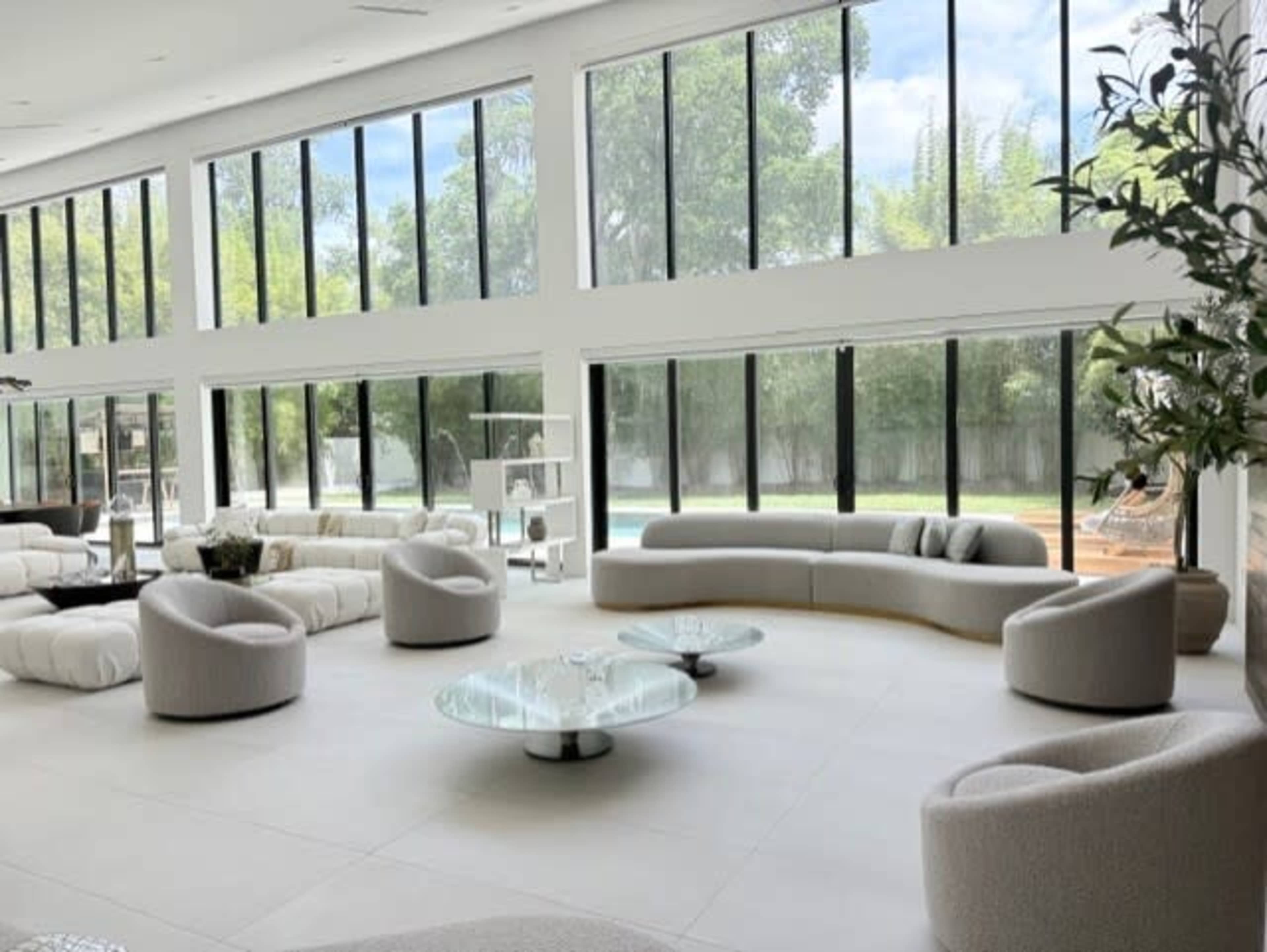 The spacious interior features modern furniture arranged around a glass coffee table, with large windows allowing natural light to illuminate the room.