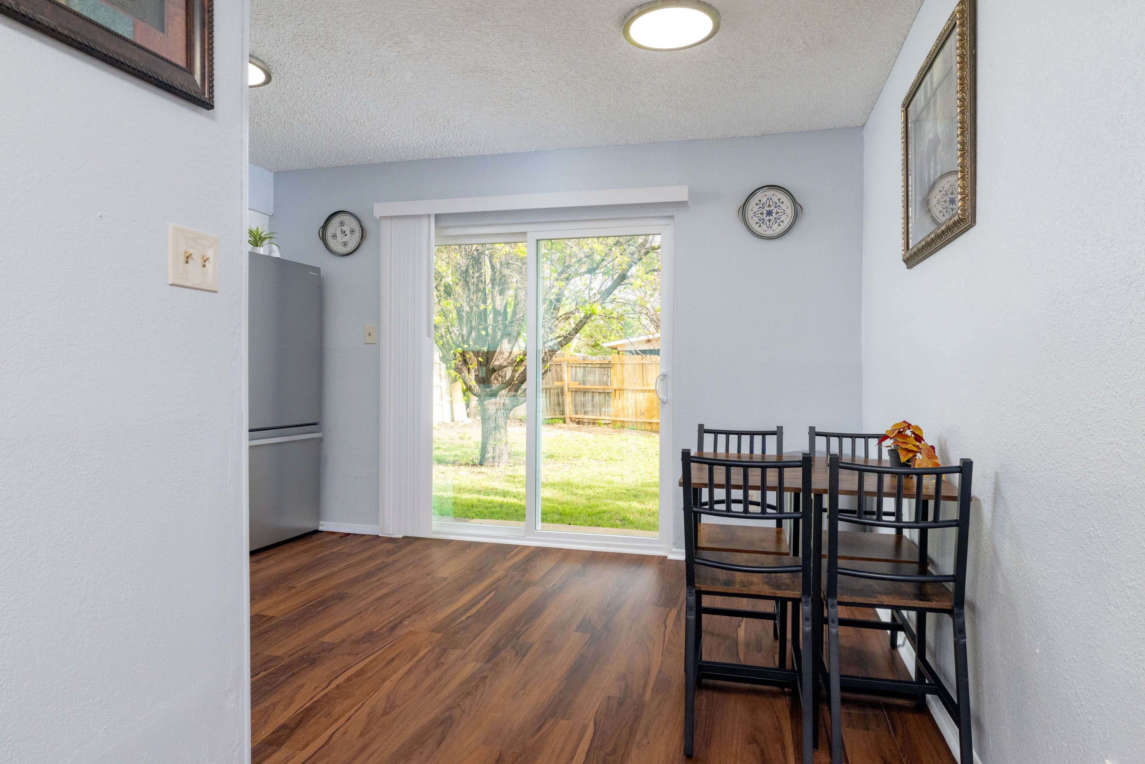 A small dining area features a table with two chairs, a sliding glass door leading to a backyard, and a refrigerator in the corner.