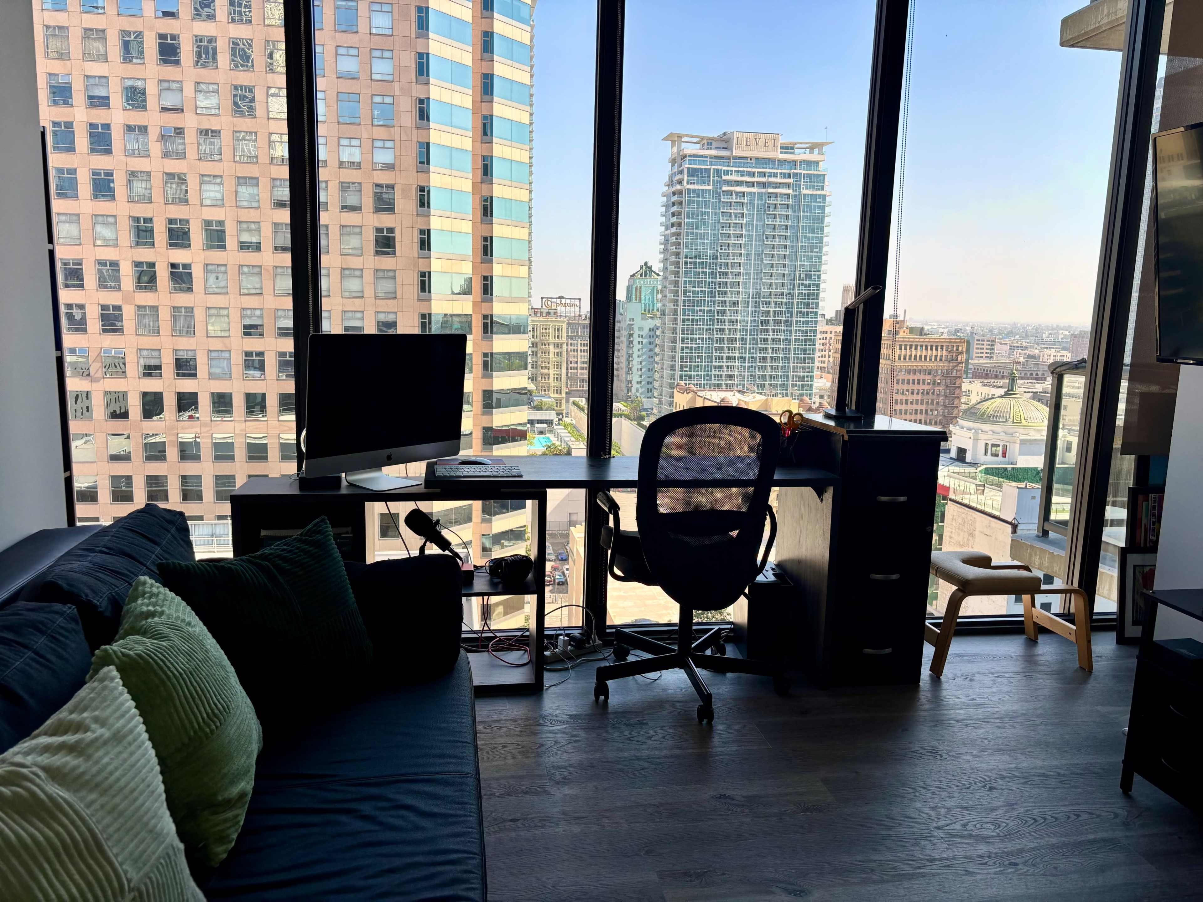 A modern office space with a desk, computer, and chair overlooks a city skyline through large windows.