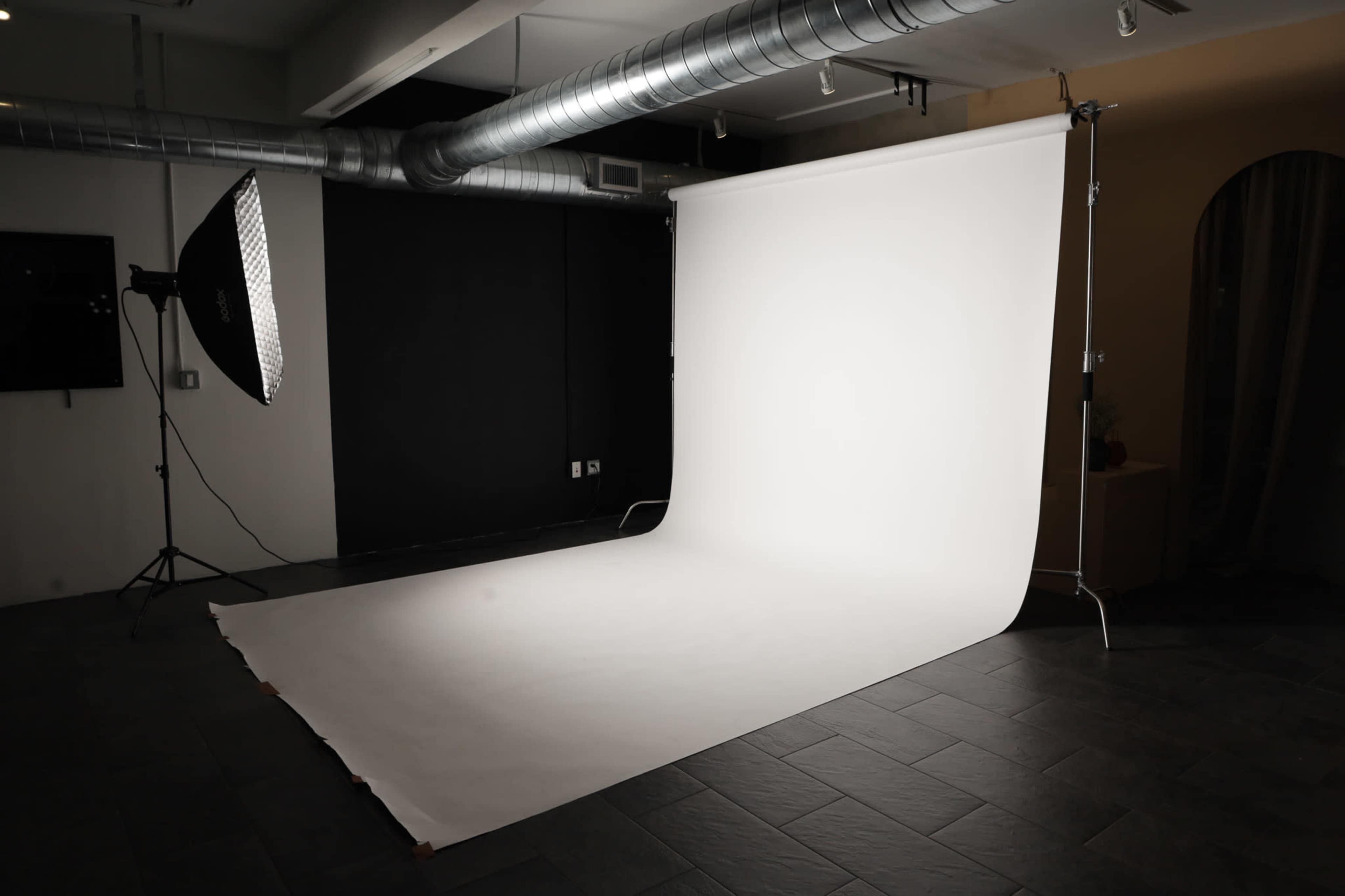 A photography studio with a white backdrop, softbox lighting, and a dark wall.