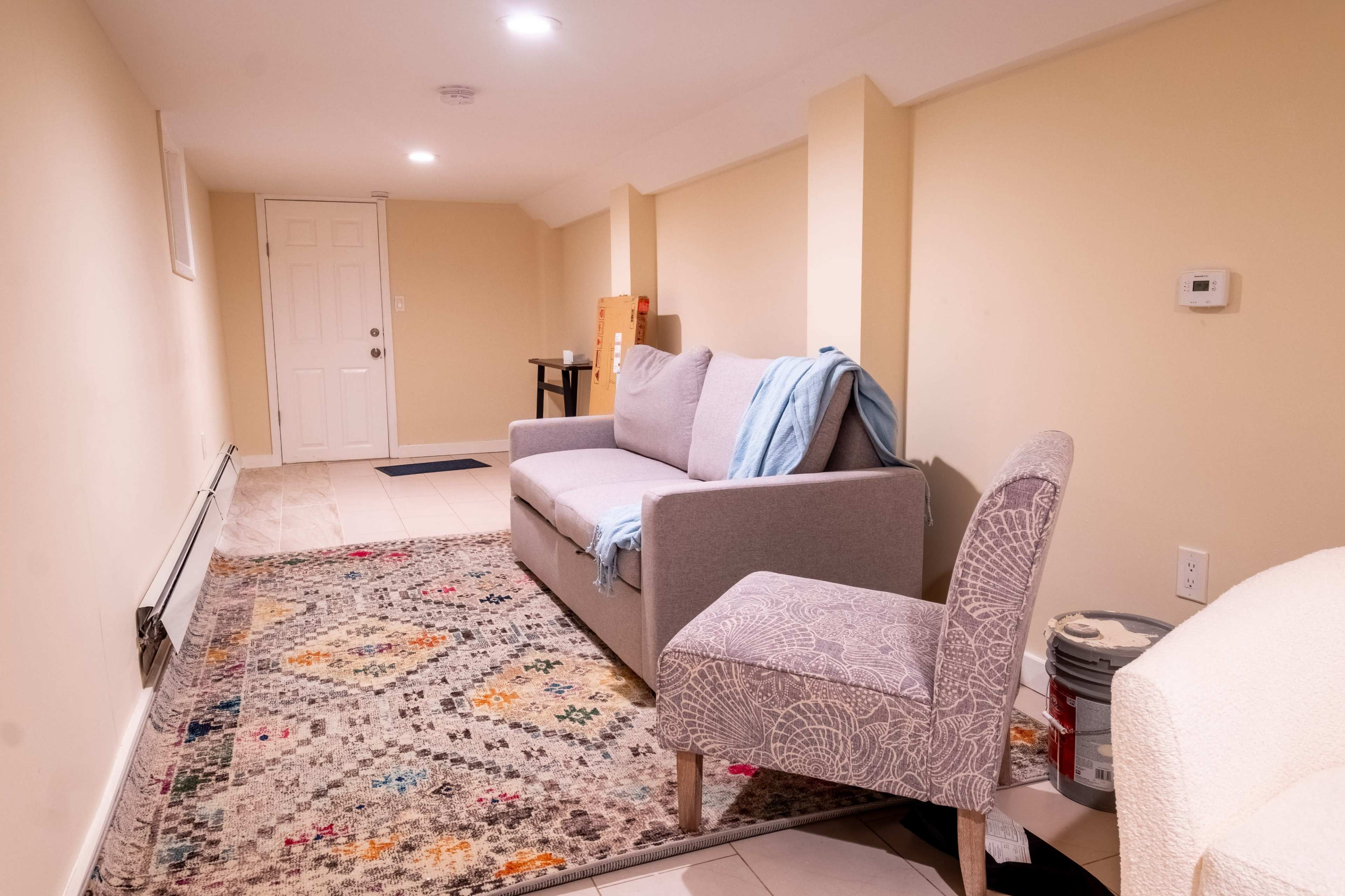 A tastefully furnished basement living area with a gray sofa, a patterned rug, and a light-colored chair.