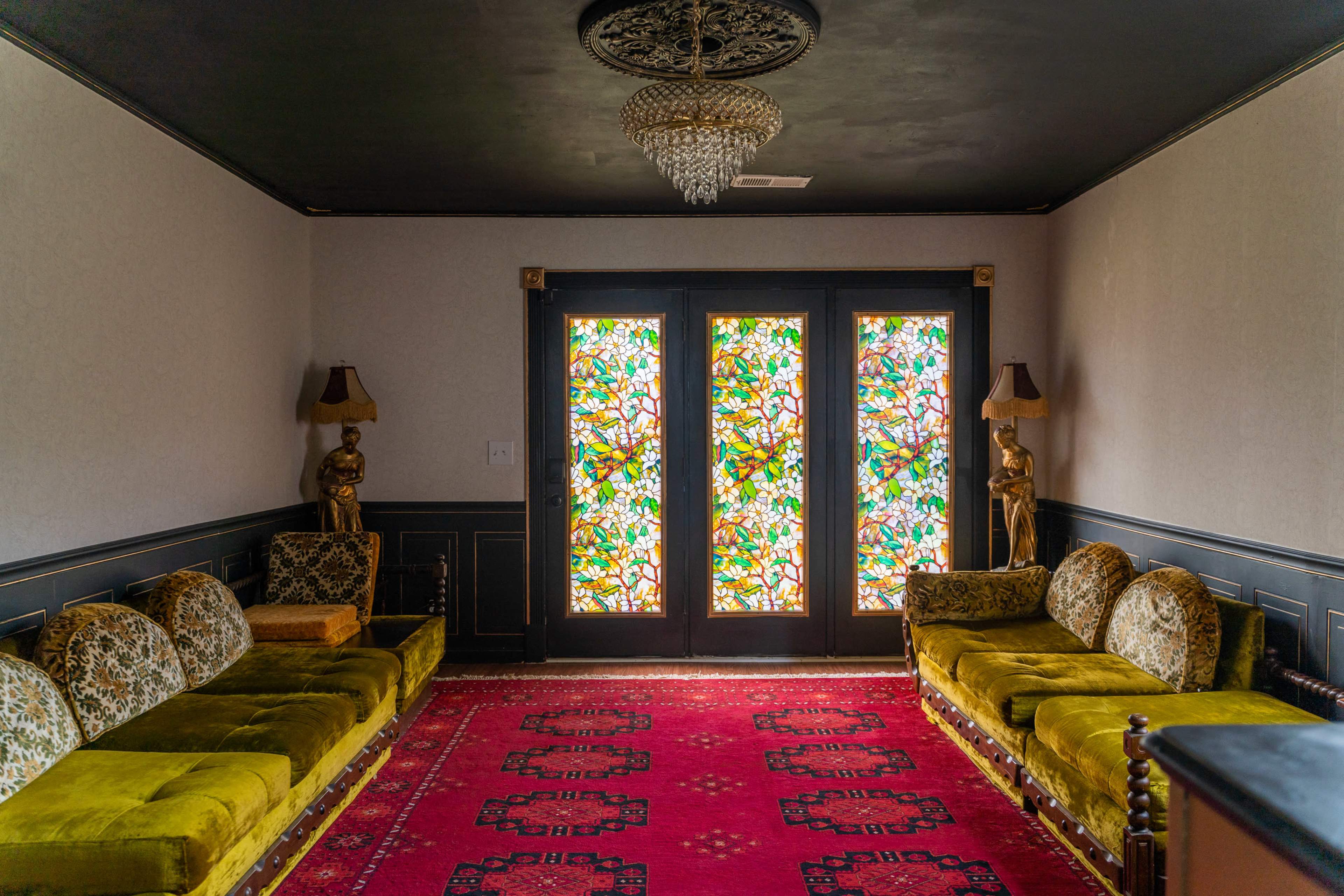 The room features a red carpet, green velvet sofas, and ornate stained glass doors adorned with intricate designs.