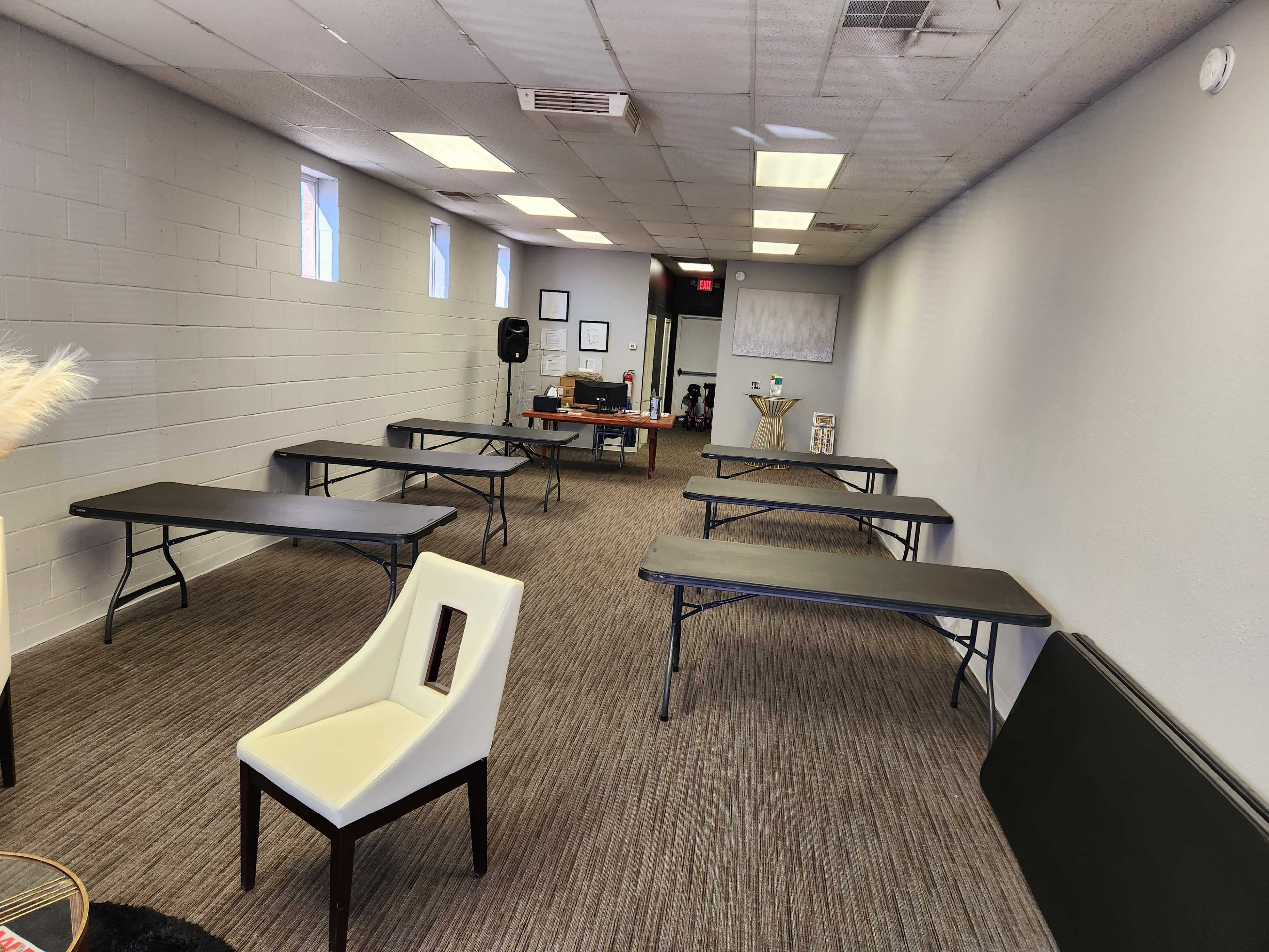 A long, narrow room with several folding tables arranged in rows and a desk at the far end.