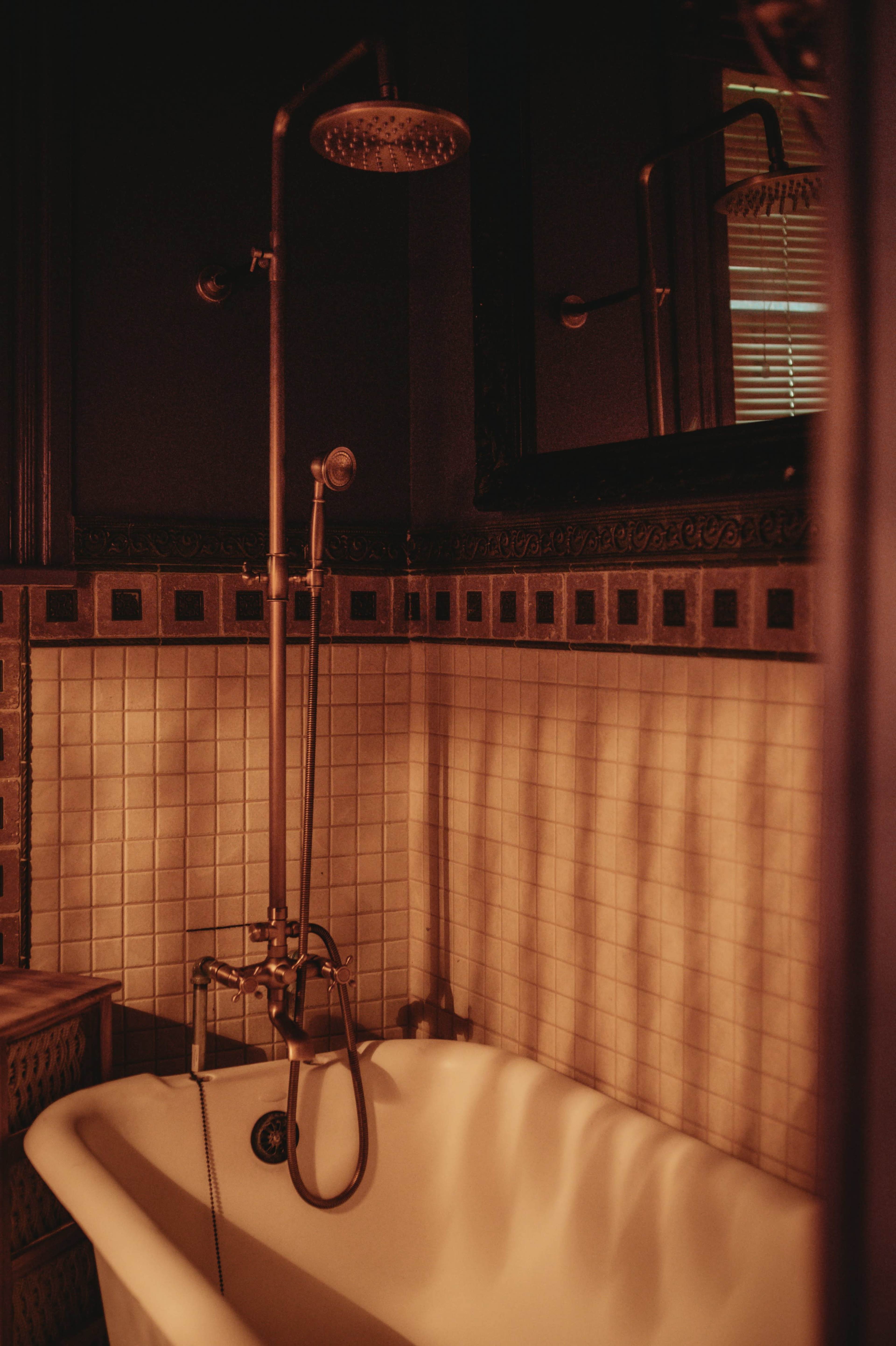The image shows a vintage bathroom featuring a freestanding bathtub, a vintage shower fixture, and tiled walls with a decorative border.