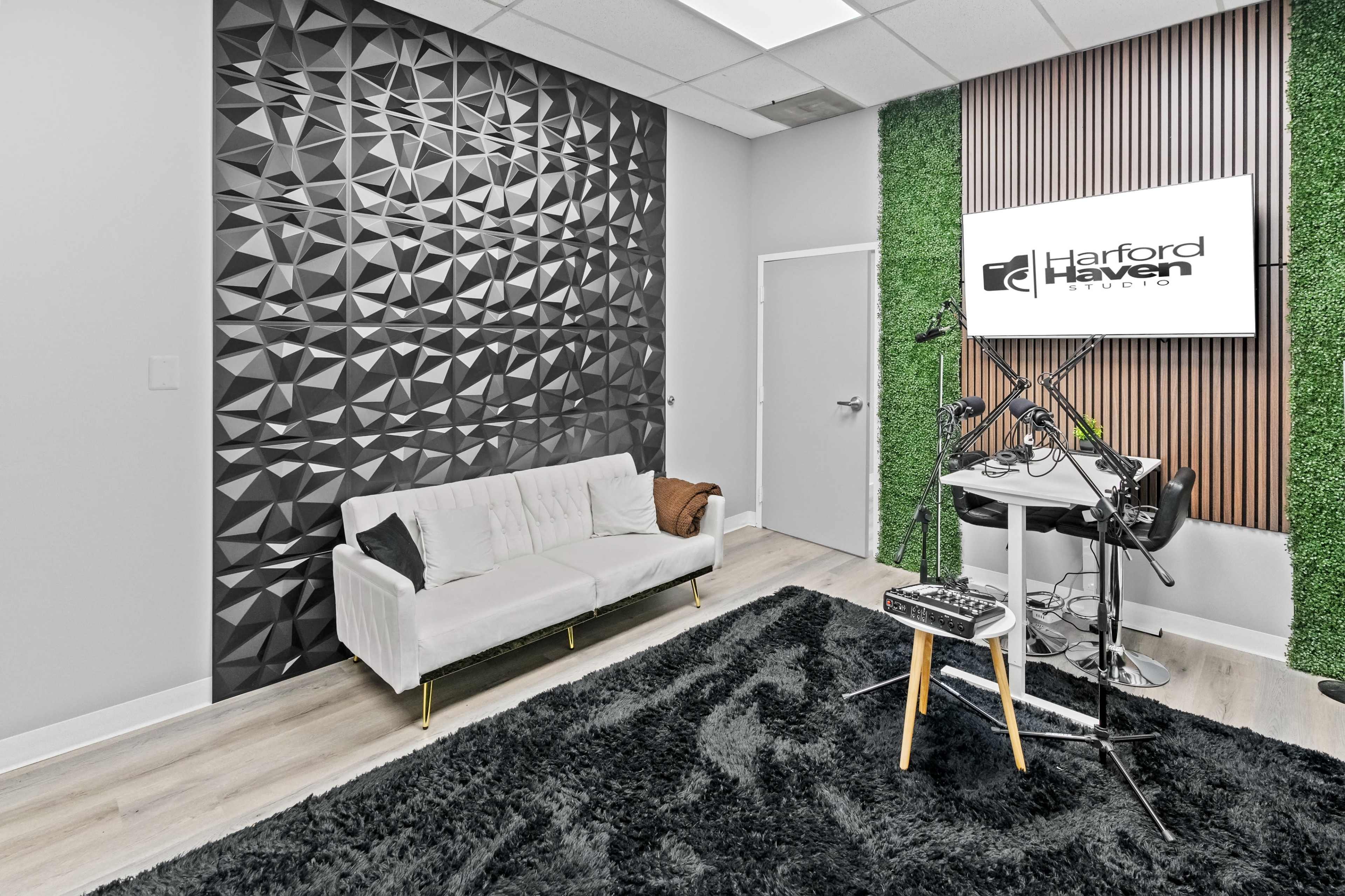 A modern studio space featuring a textured black wall, a white sofa, a green accent wall, and equipment on a small table.