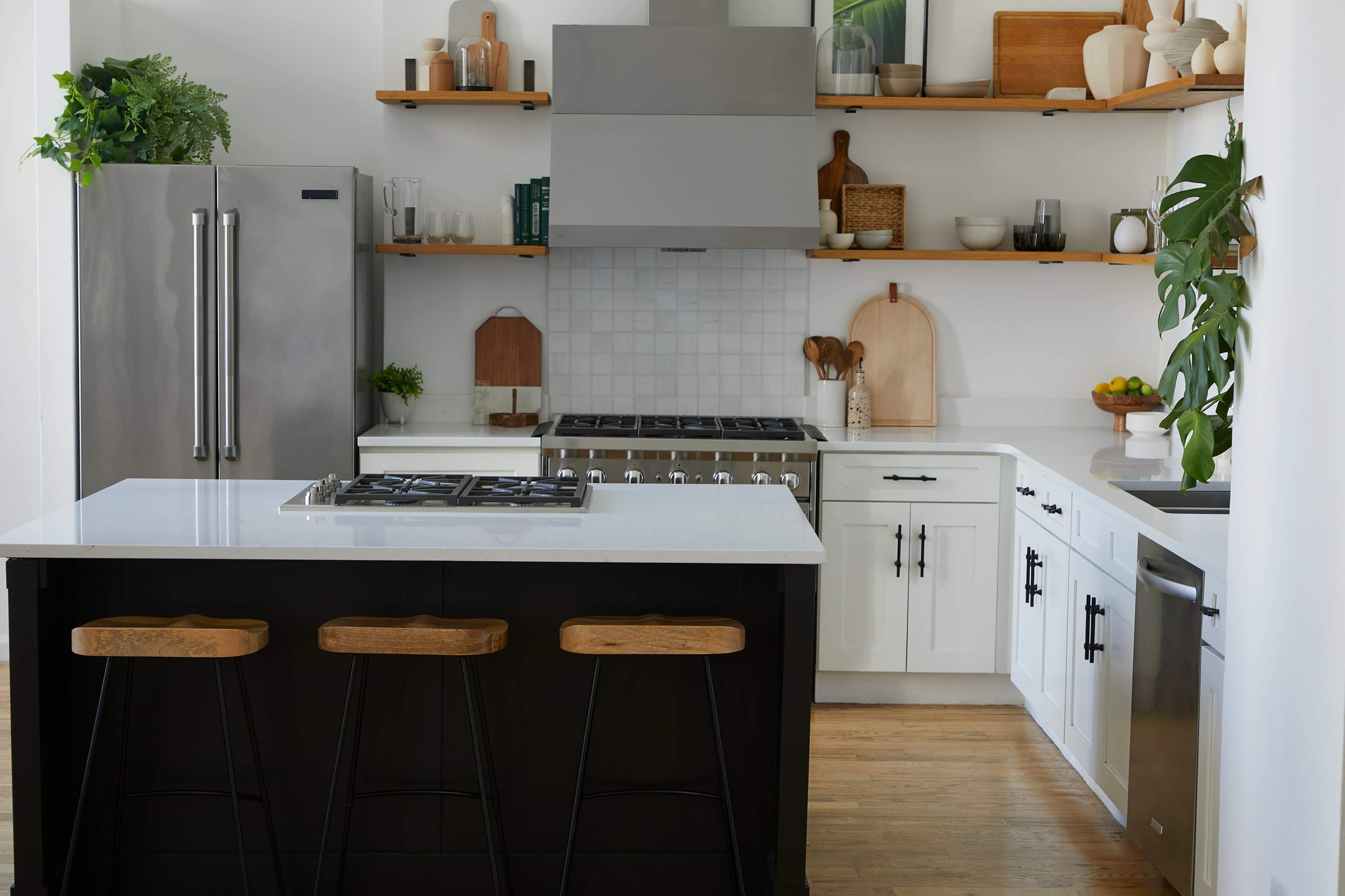 A modern kitchen features a central island with bar stools, stainless steel appliances, and open shelving displaying kitchenware.