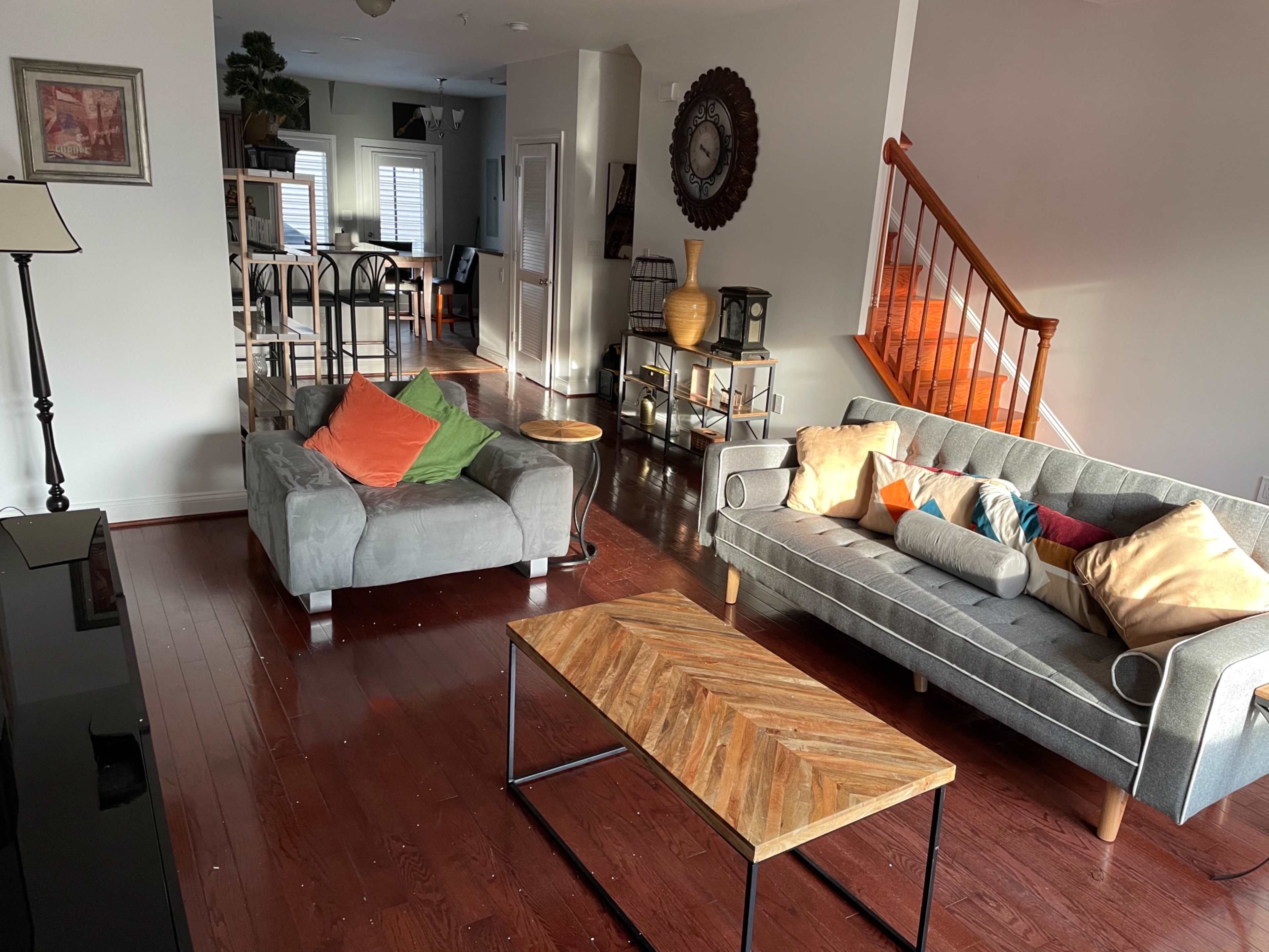 The living room features two sofas with colorful cushions, a wooden coffee table, and a staircase leading to an upper level.