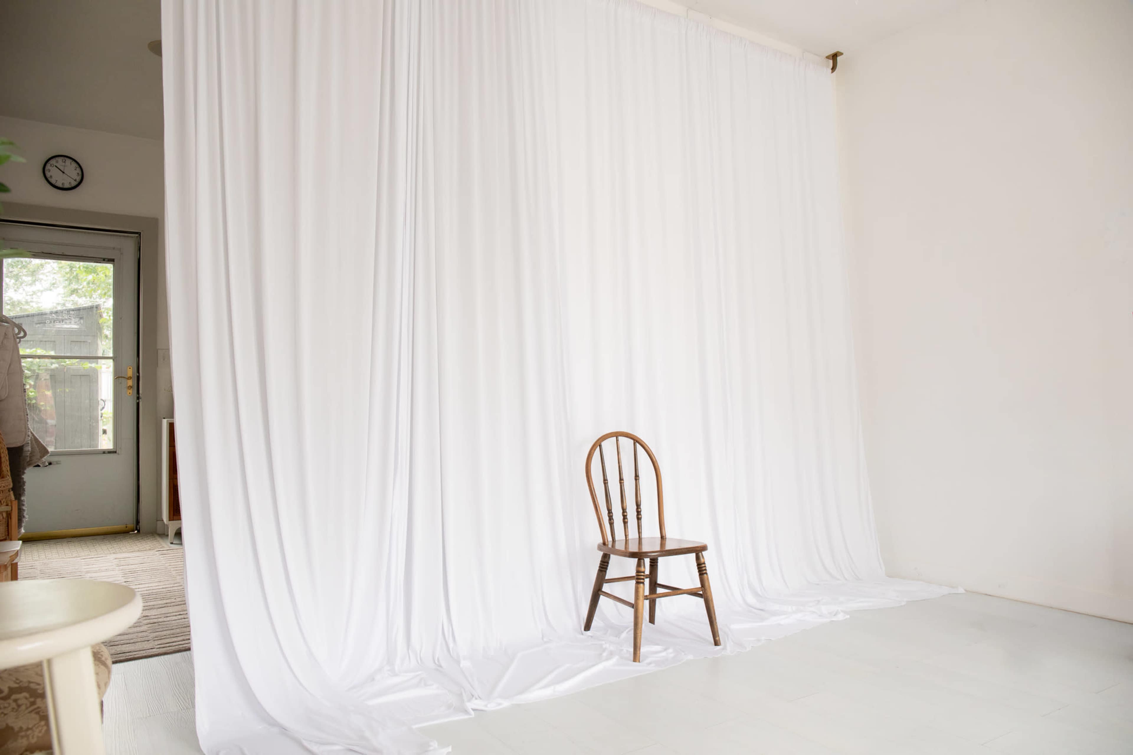 The image shows a simple interior space with a white backdrop and a single wooden chair in front of it.