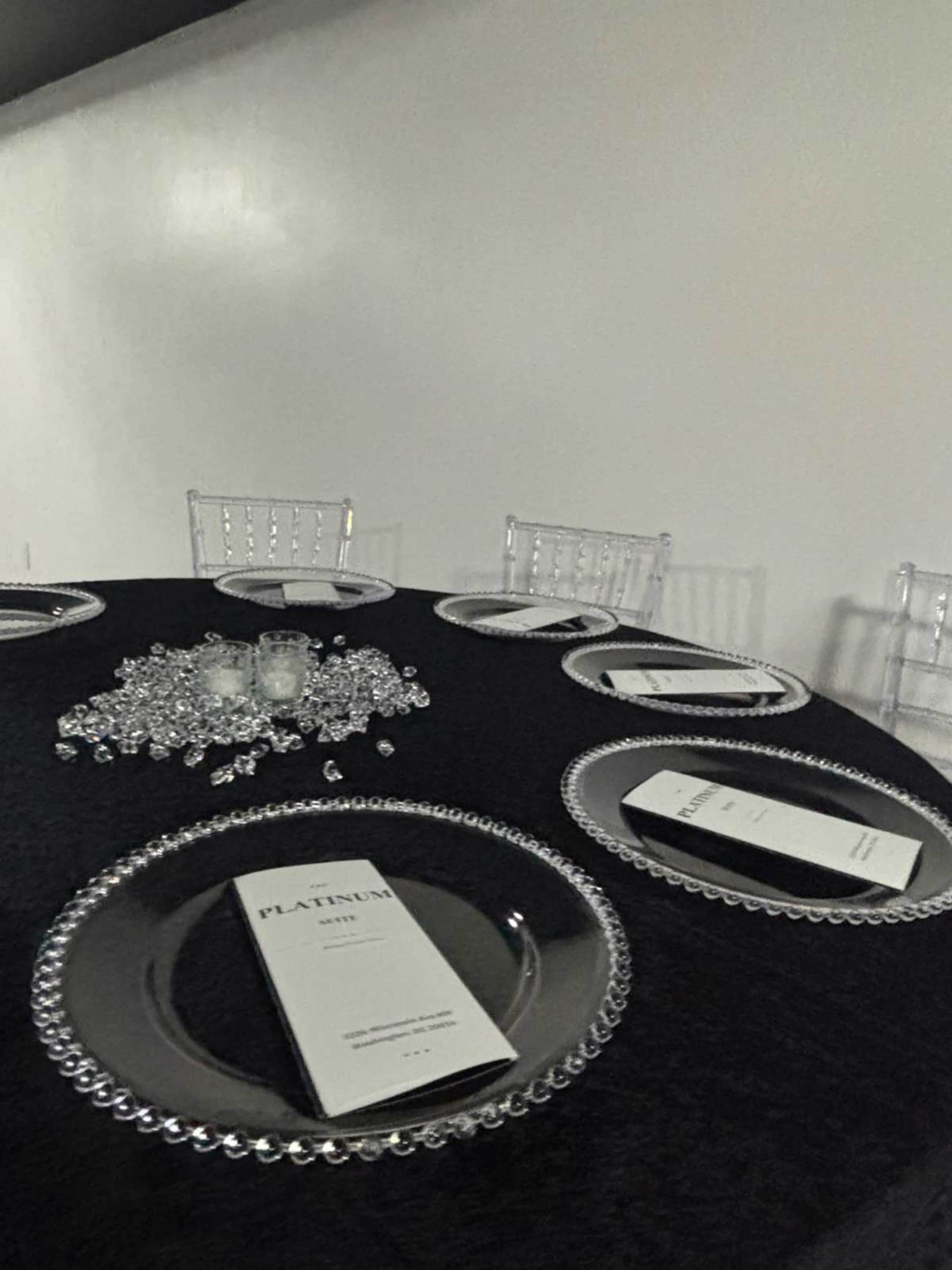 A round table is set with silver chargers, neatly arranged menus, and decorative crystals, all against a black tablecloth.