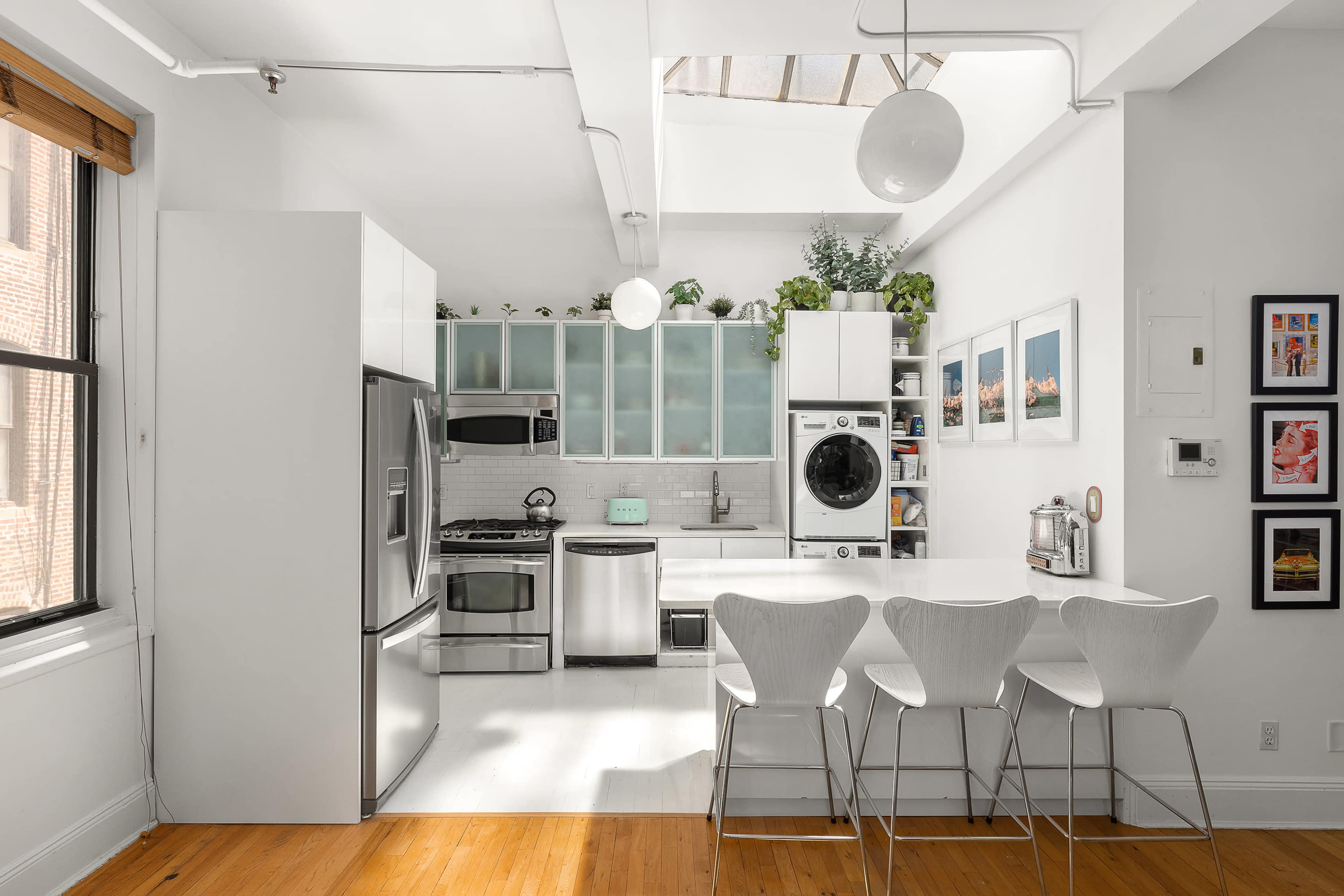 The image shows a modern kitchen with stainless steel appliances, white cabinetry, and a small dining area featuring four white chairs.