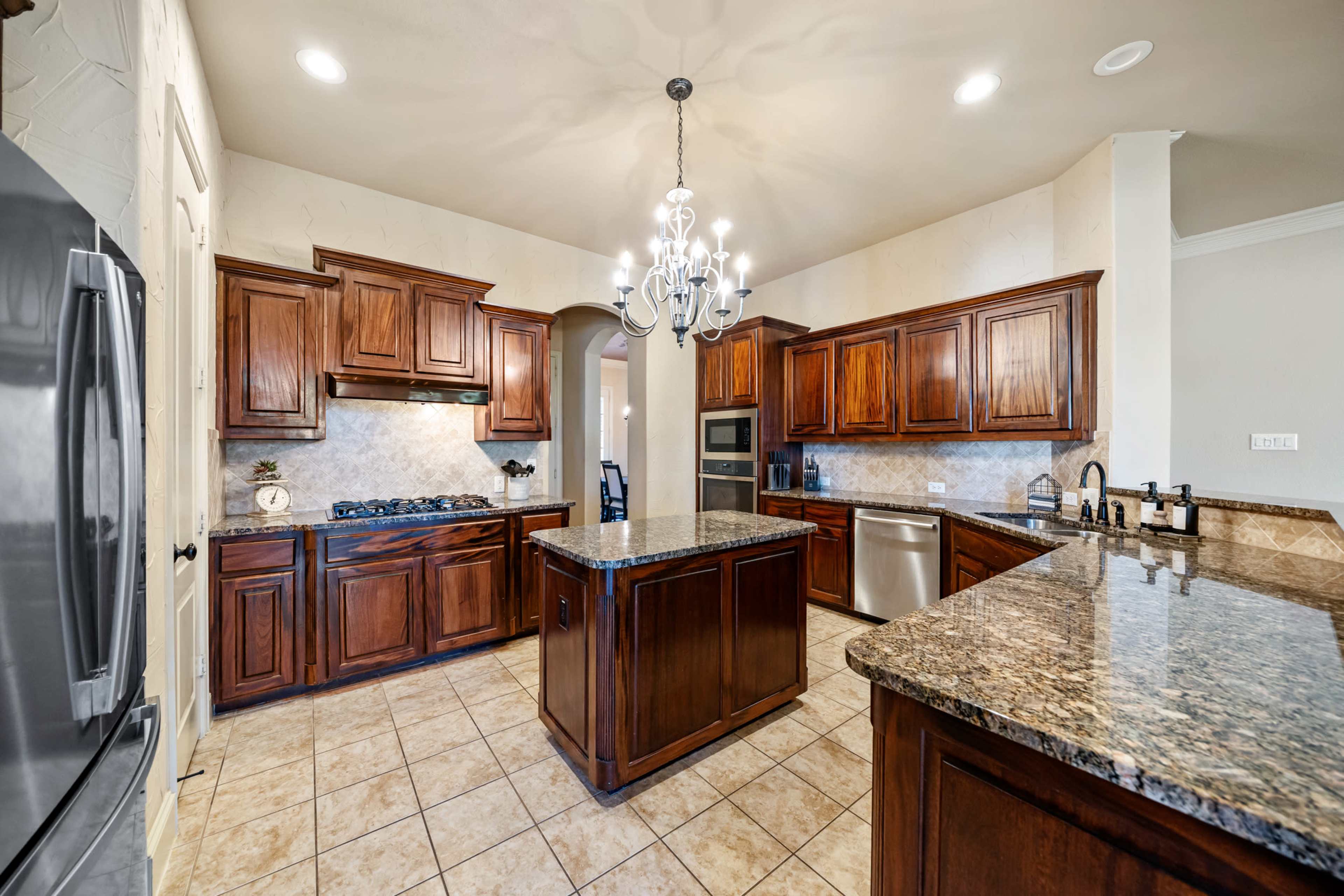 The kitchen features wooden cabinetry, granite countertops, and a large central island with a chandelier above.