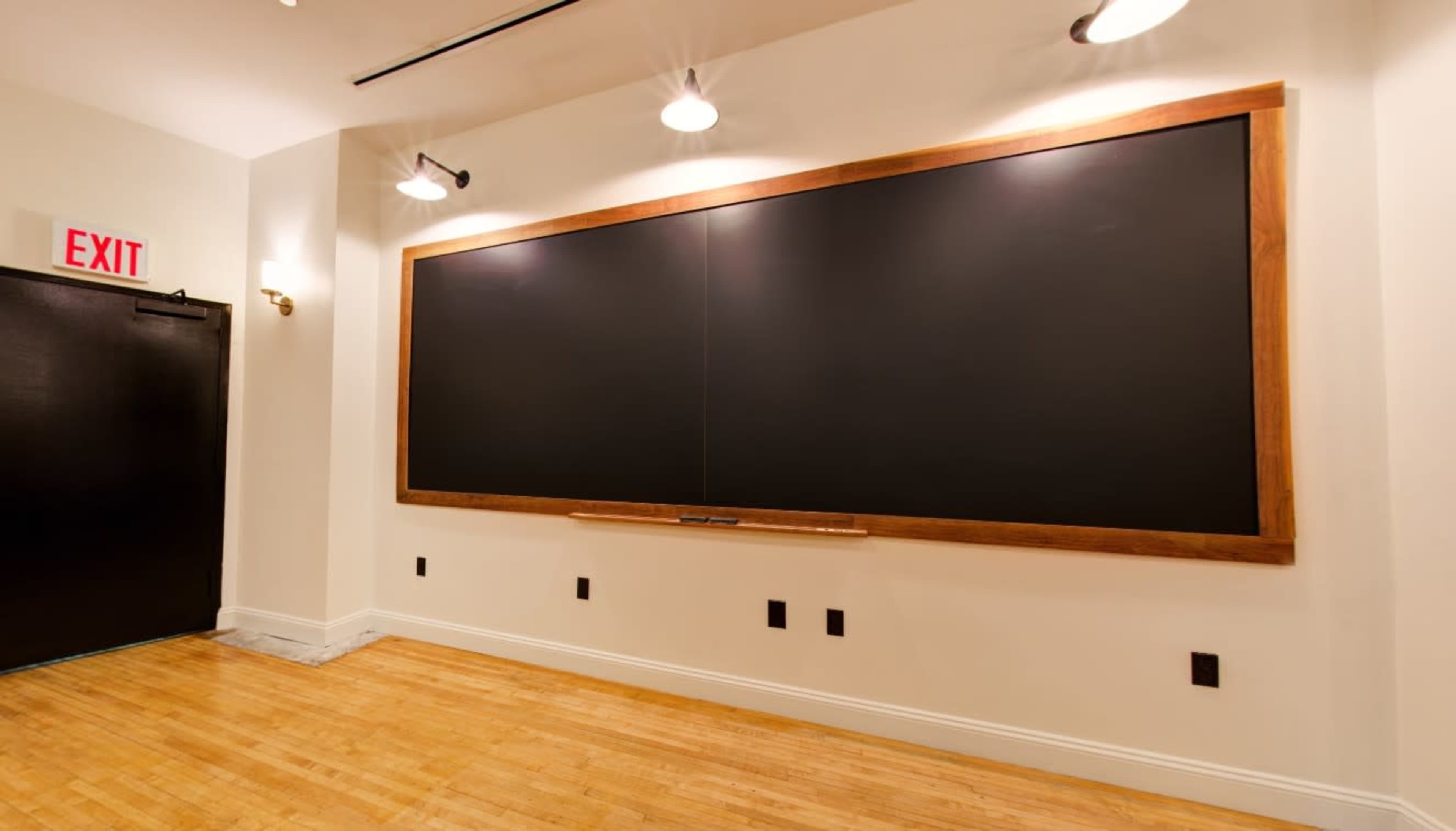 The image shows a large blackboard mounted on a wall in a well-lit room with wooden flooring.