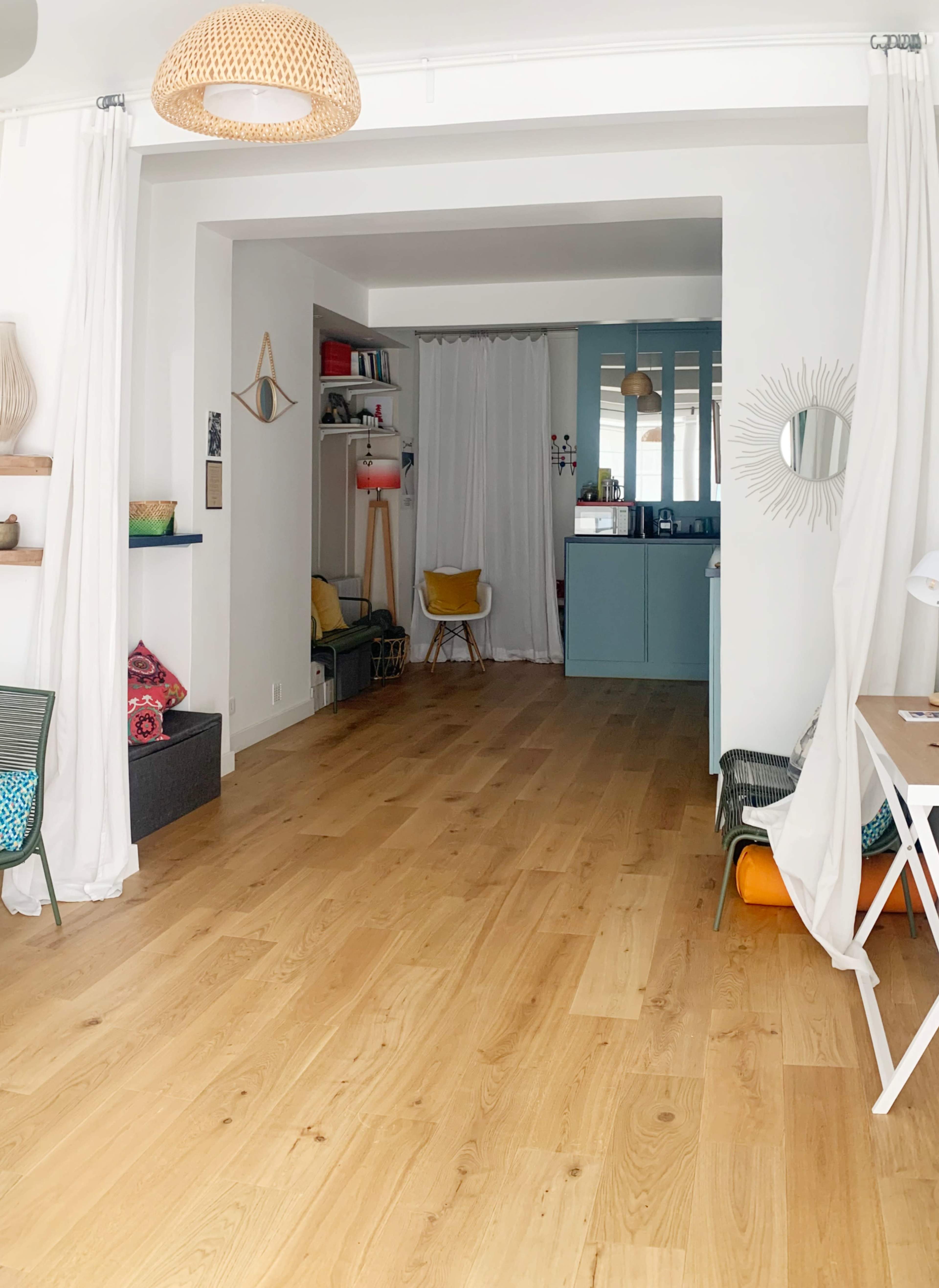 The image shows an interior space with light wood flooring, white walls, and a mix of seating areas, including chairs and a workspace.