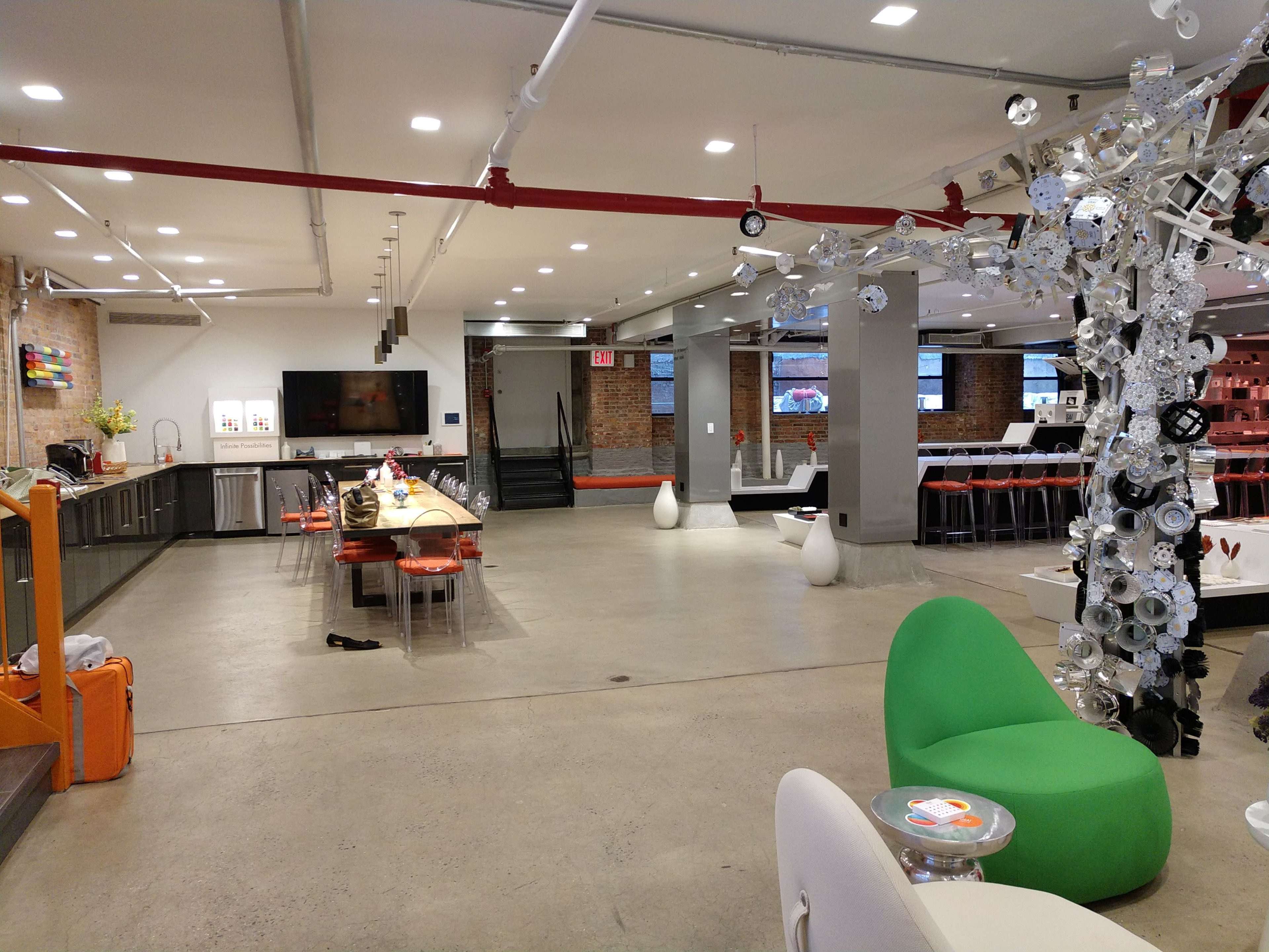 The image shows a spacious, modern interior featuring a kitchen area, seating arrangements, and decorative elements, with an emphasis on open space and industrial design.