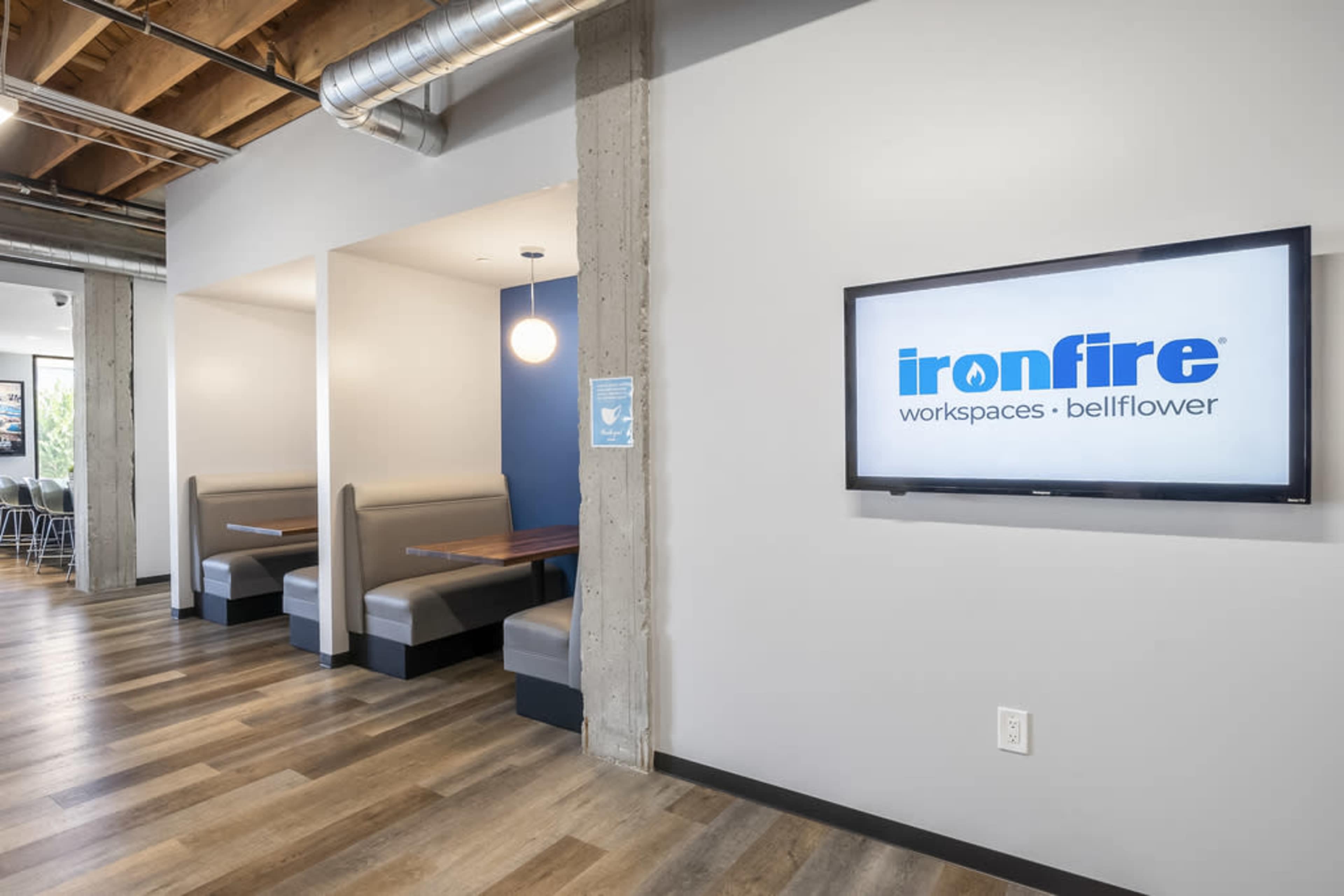 A modern workspace with booth seating and a television displaying the "ironfire workspaces: bellflower" logo on the wall.