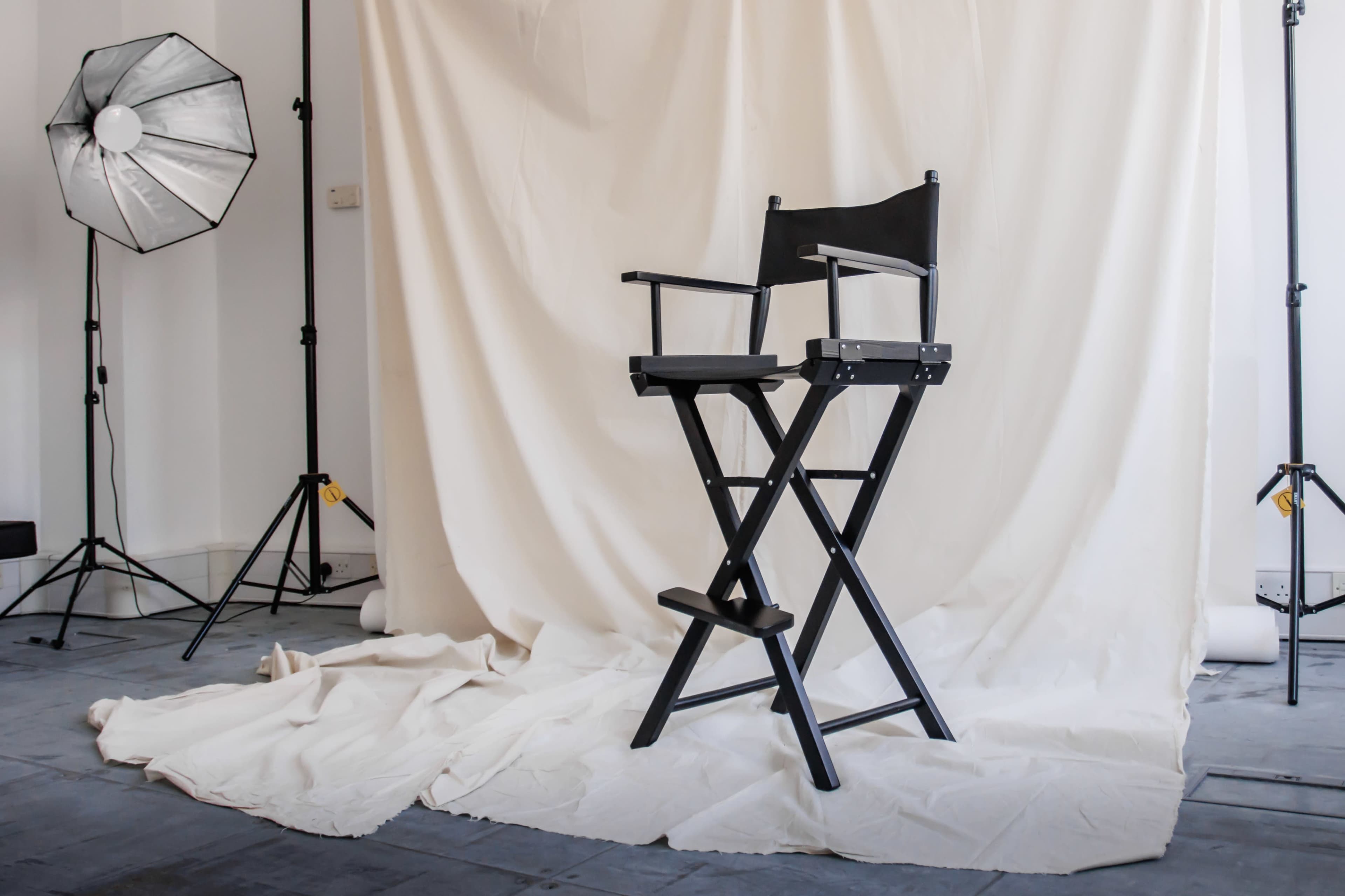 A black director's chair is positioned in front of a white backdrop in a photography studio.