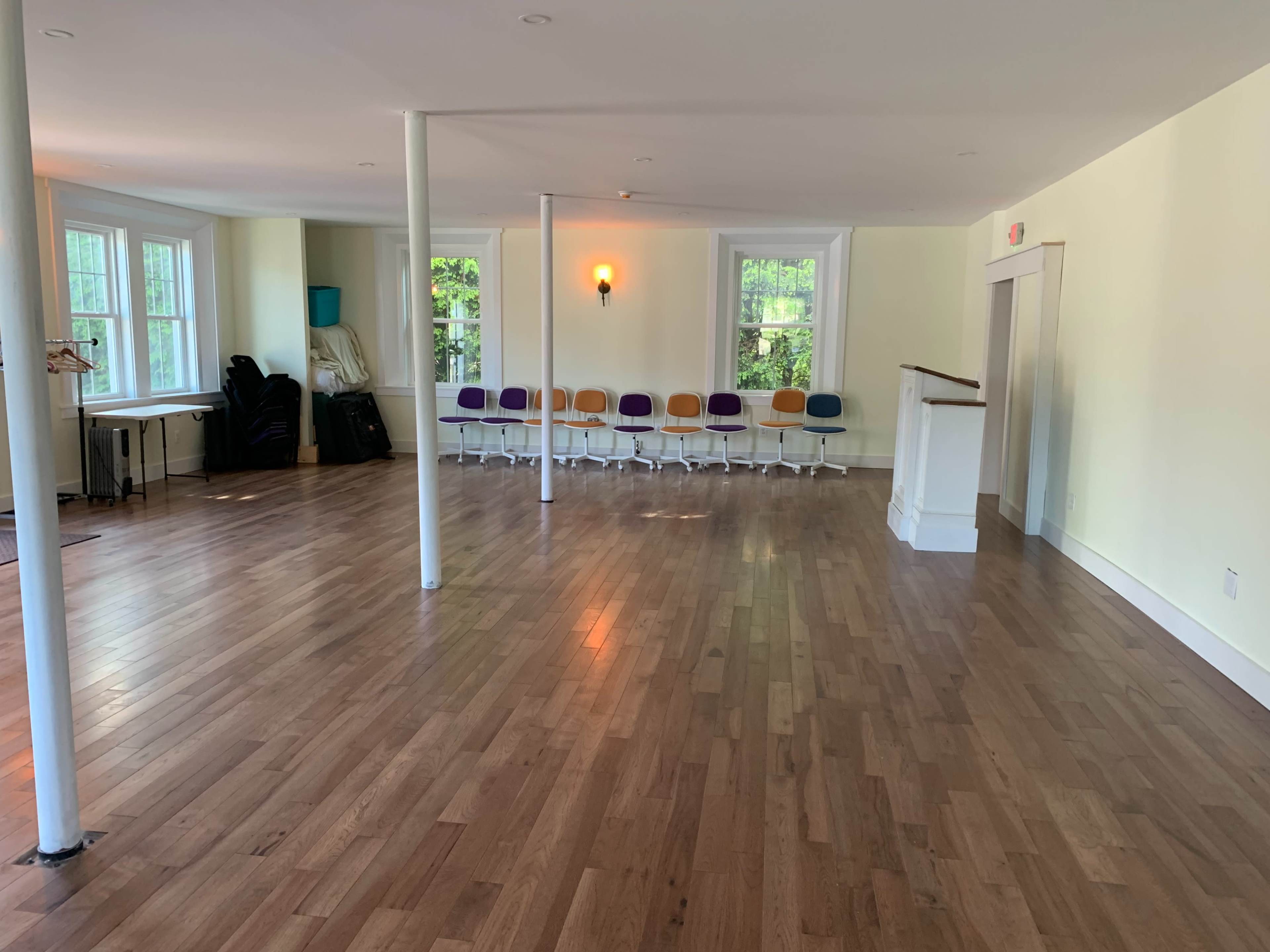 The room features polished wooden floors, white walls, and a row of colorful chairs against one wall.