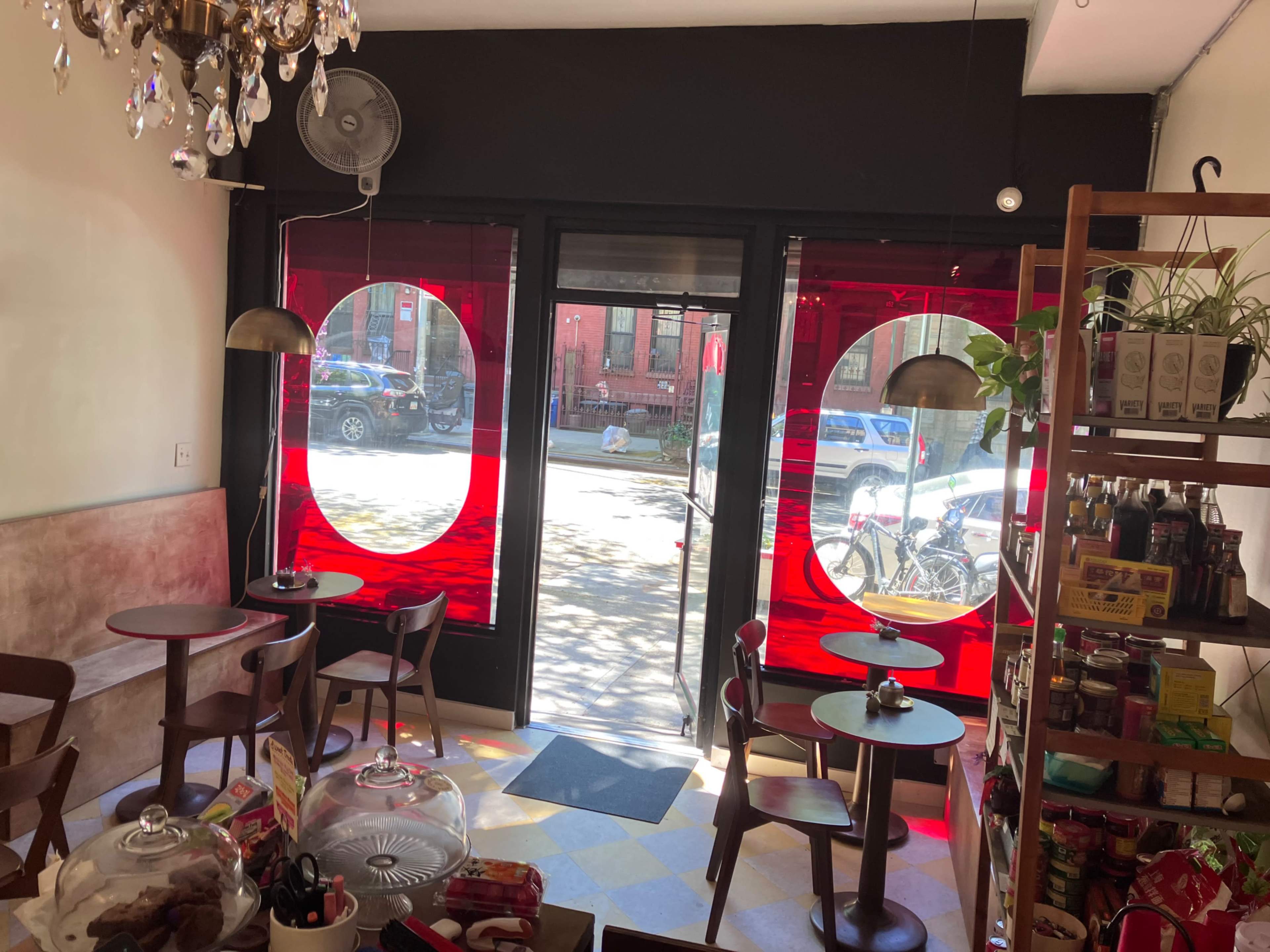 The image shows a café interior with round, red window displays, wooden tables, and a view of a street through the glass doors.