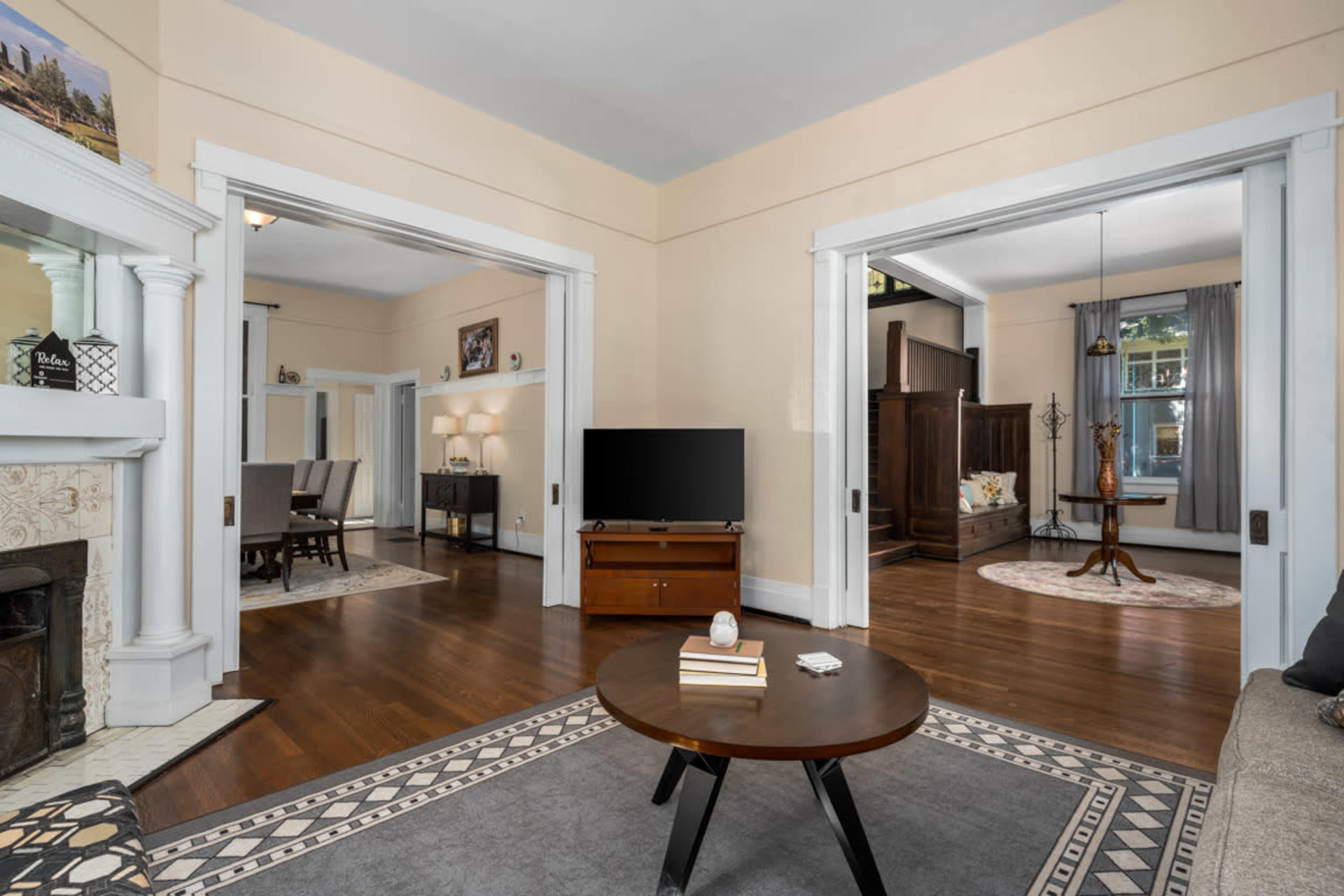 A cozy living area with two archways leading to adjoining rooms, featuring a coffee table, a television, and a fireplace.