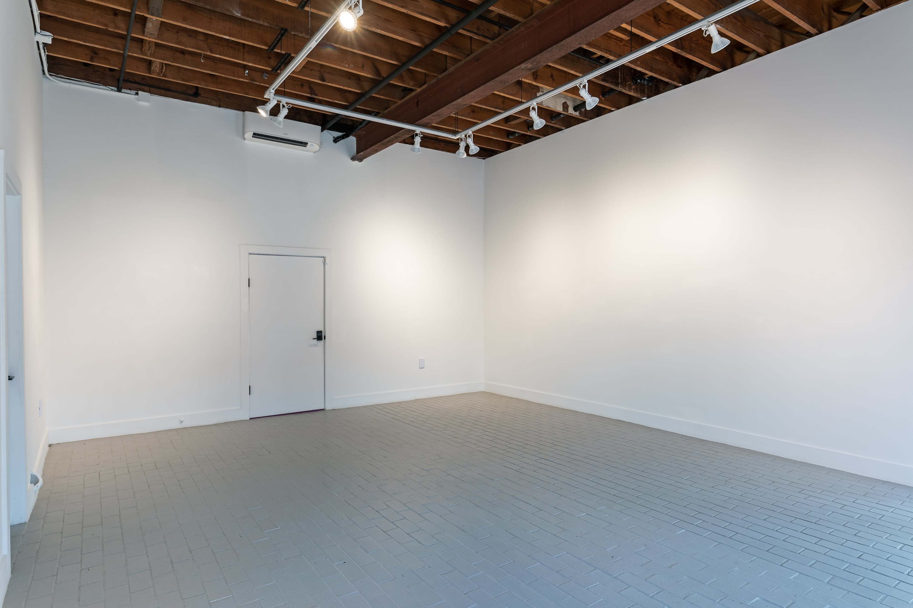 A vacant room with a light gray tiled floor, white walls, and a brown wooden ceiling with track lighting.