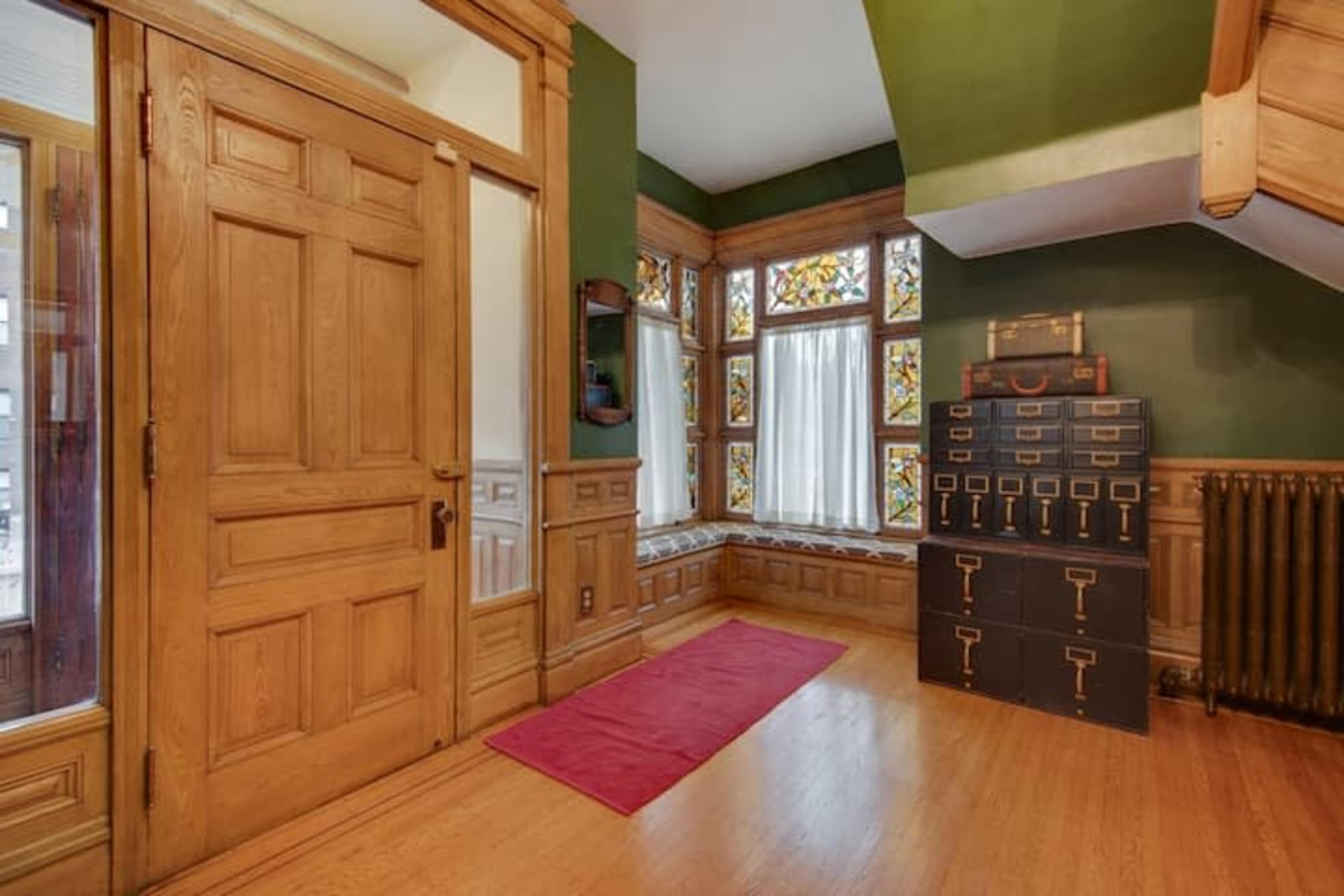 A wooden entryway with a colorful stained glass window and a black filing cabinet near a staircase.