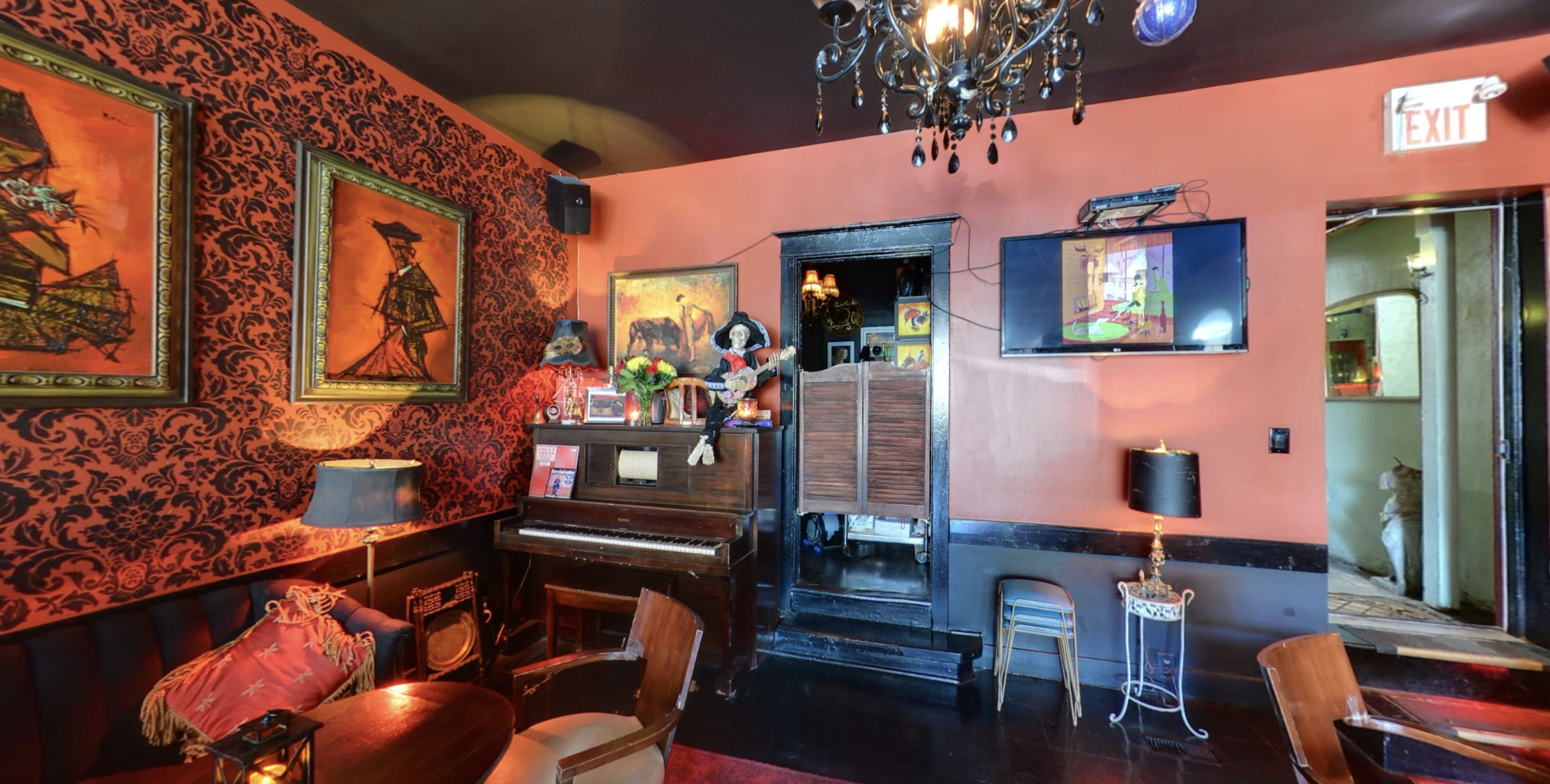 The interior of a dimly lit bar features vintage decor, a piano, wall art, and a television, creating an inviting atmosphere.