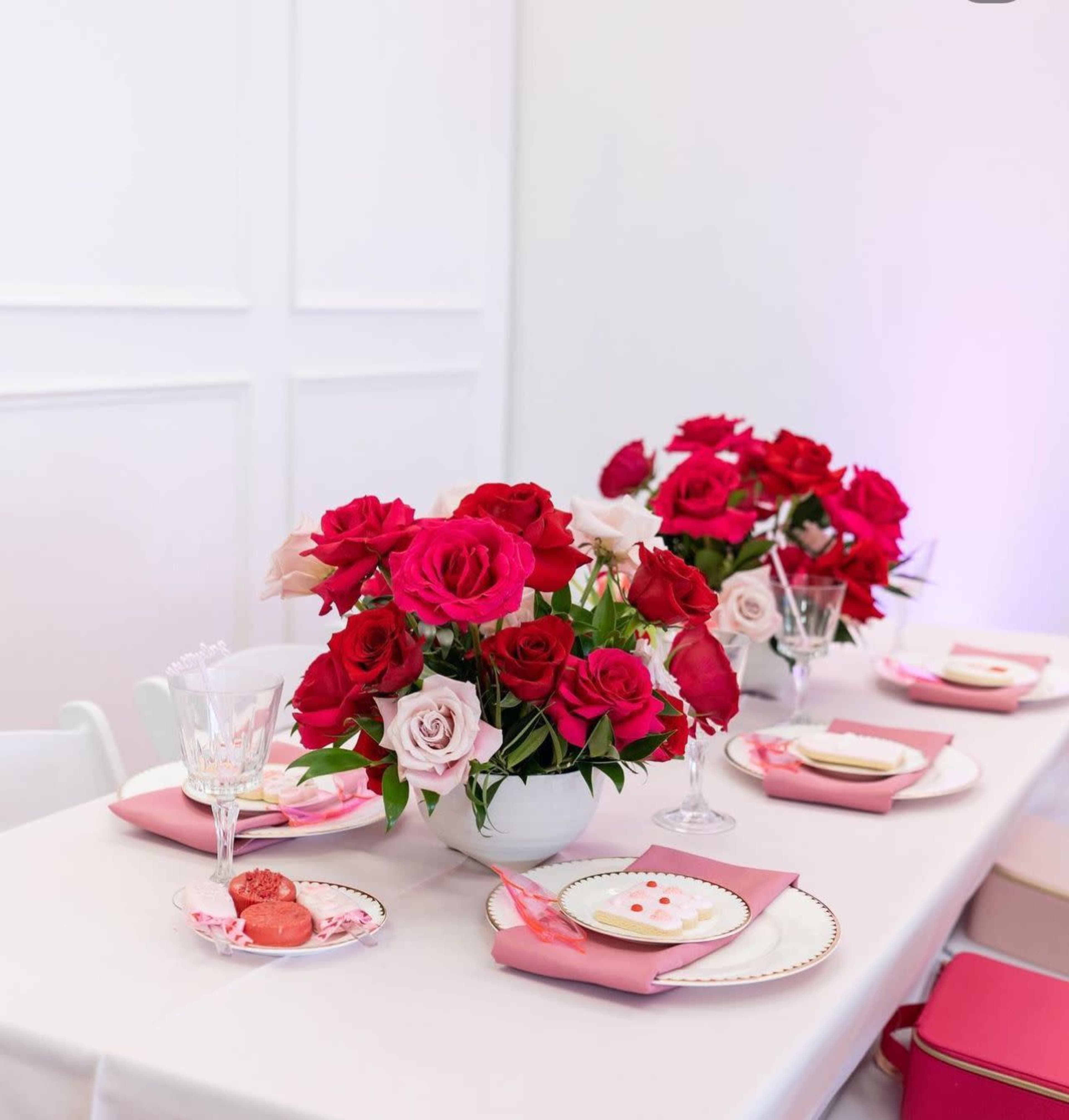 A table is set with pink and white tableware, featuring two large flower arrangements of red and white roses at the center.