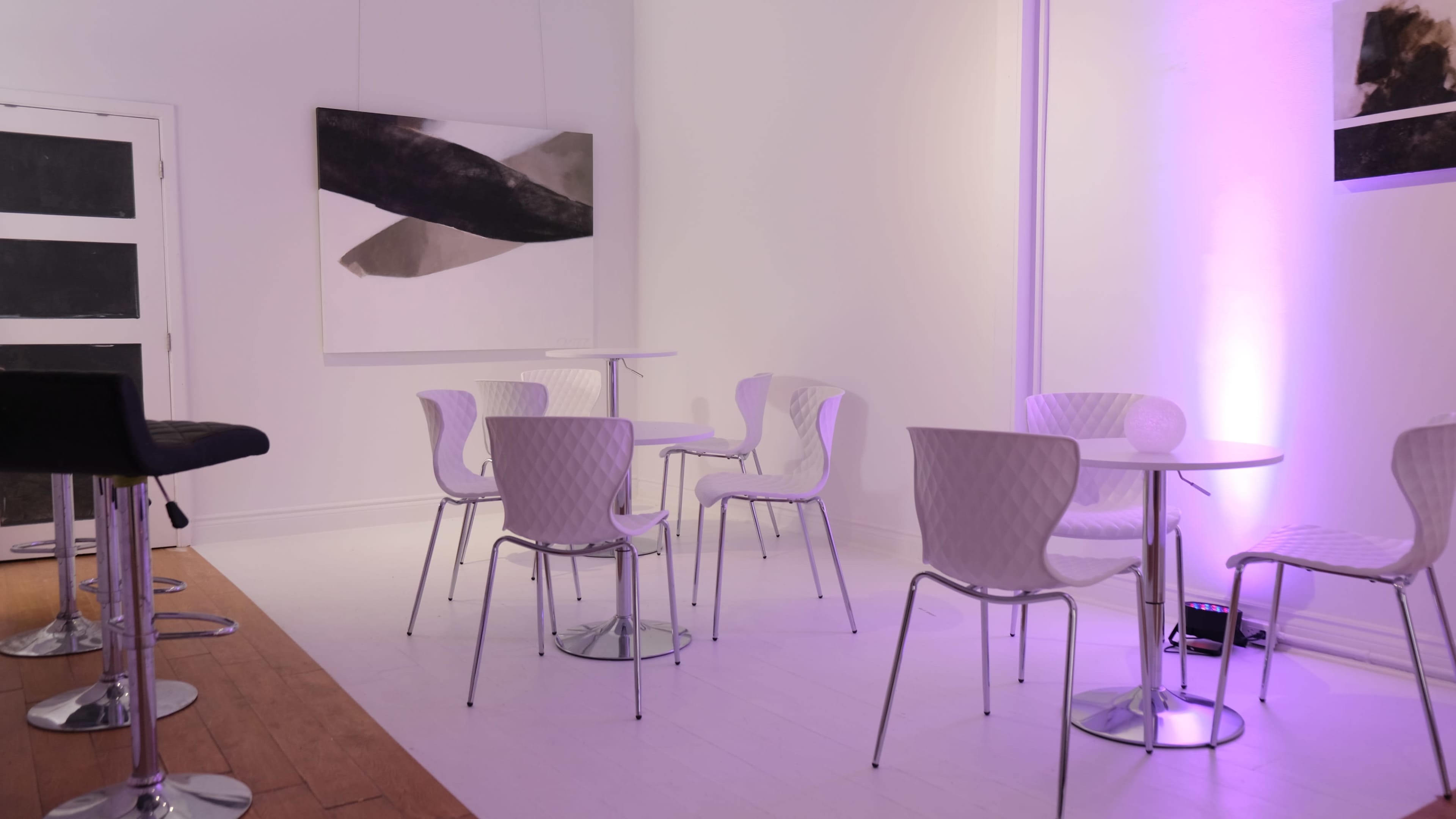 A minimalist and bright interior with purple lighting, featuring several white chairs and tables, alongside a large abstract artwork on the wall.