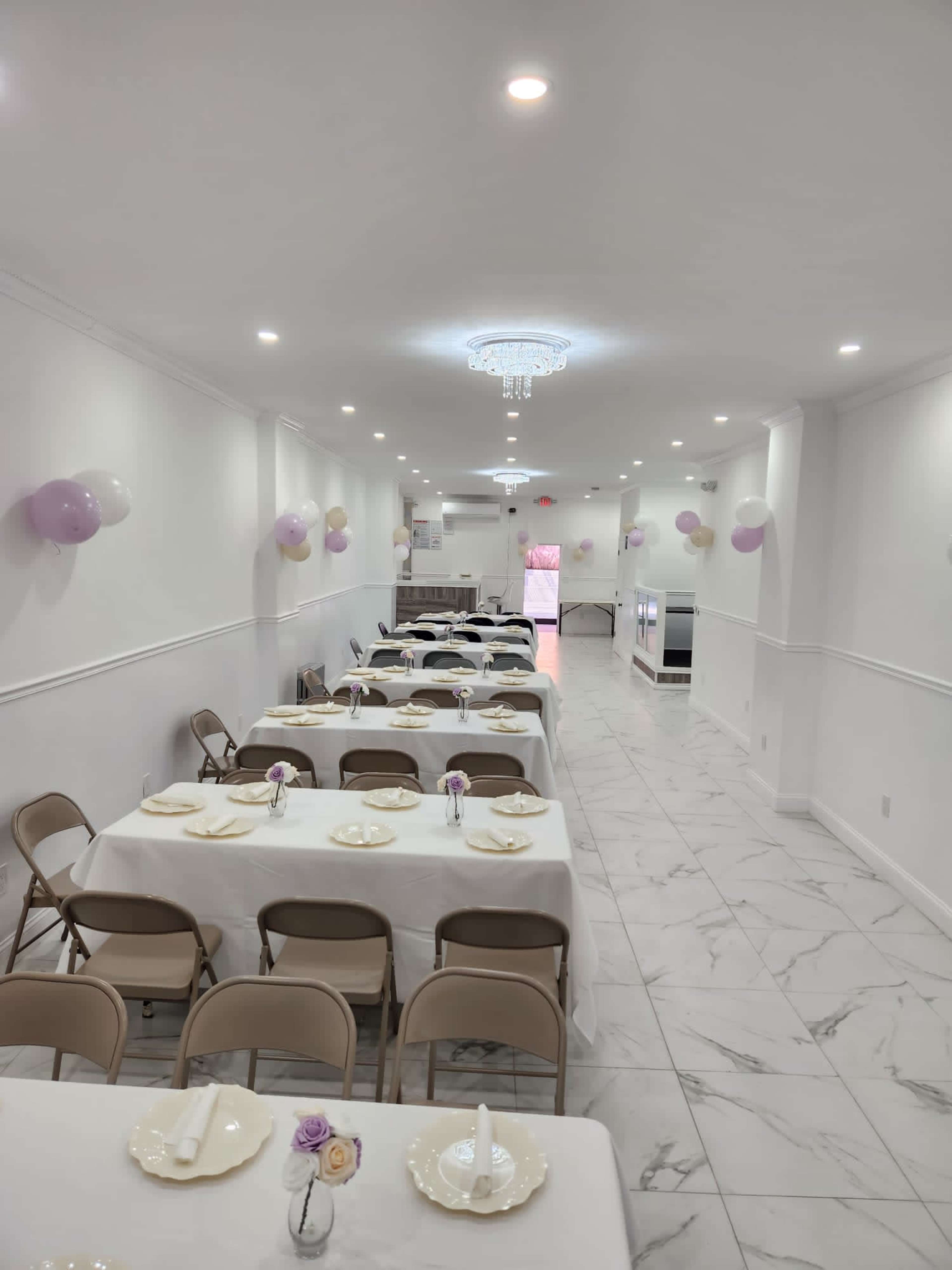 A long, narrow banquet hall with neatly arranged tables covered in white tablecloths and decorated with small floral centerpieces.