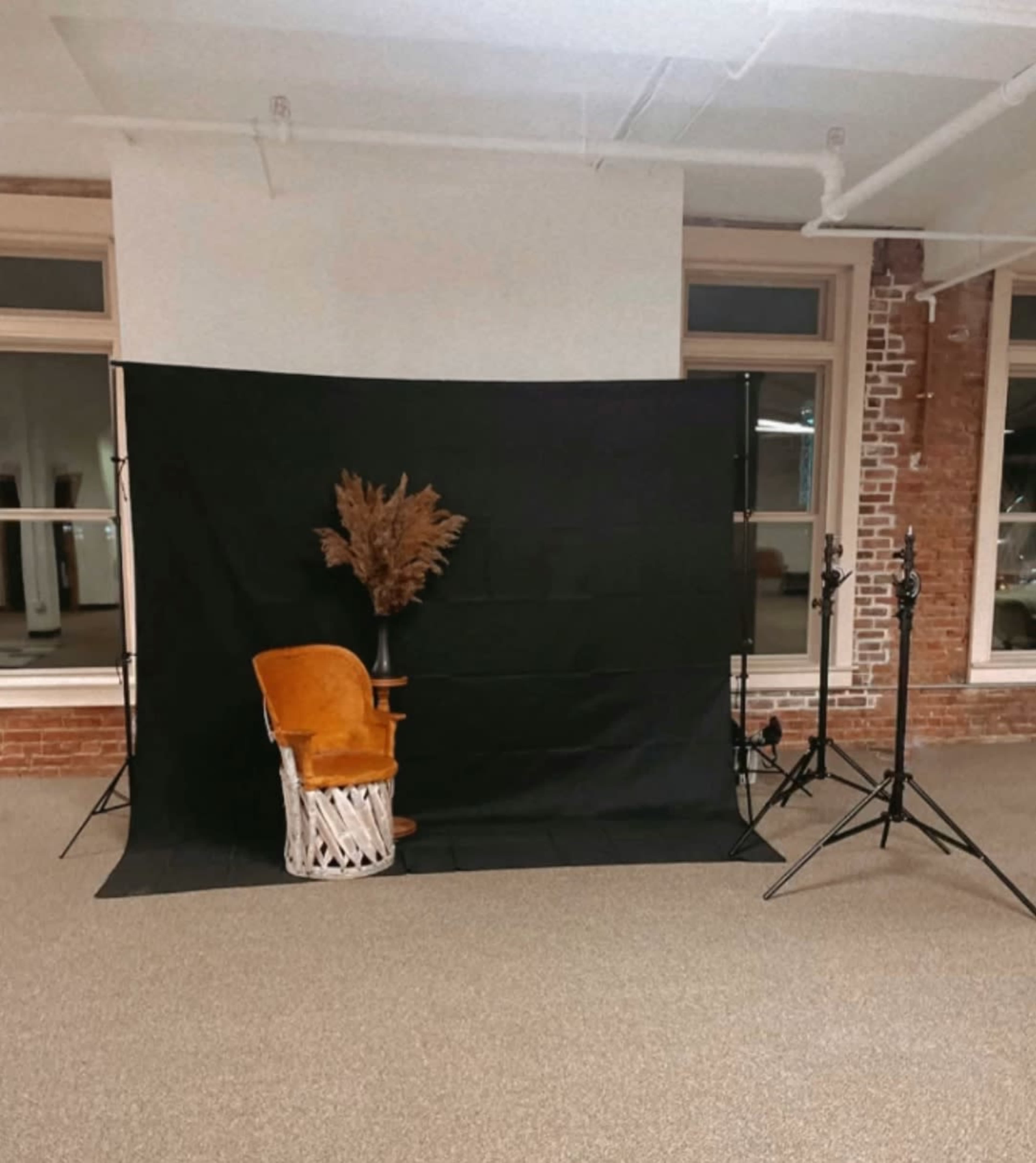 The image shows a photo setup featuring a wooden chair with a yellow cushion positioned in front of a black backdrop, with two light stands on either side.