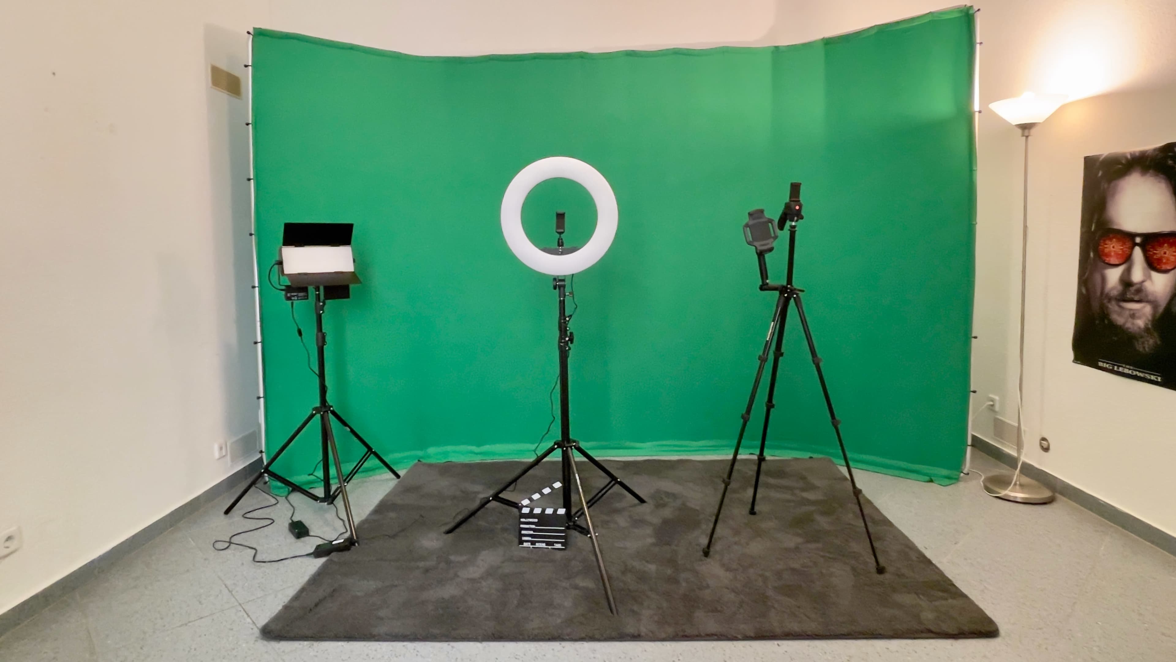 The image shows a photography setup featuring a green backdrop, a ring light, a softbox light, and multiple tripods on a carpeted floor.