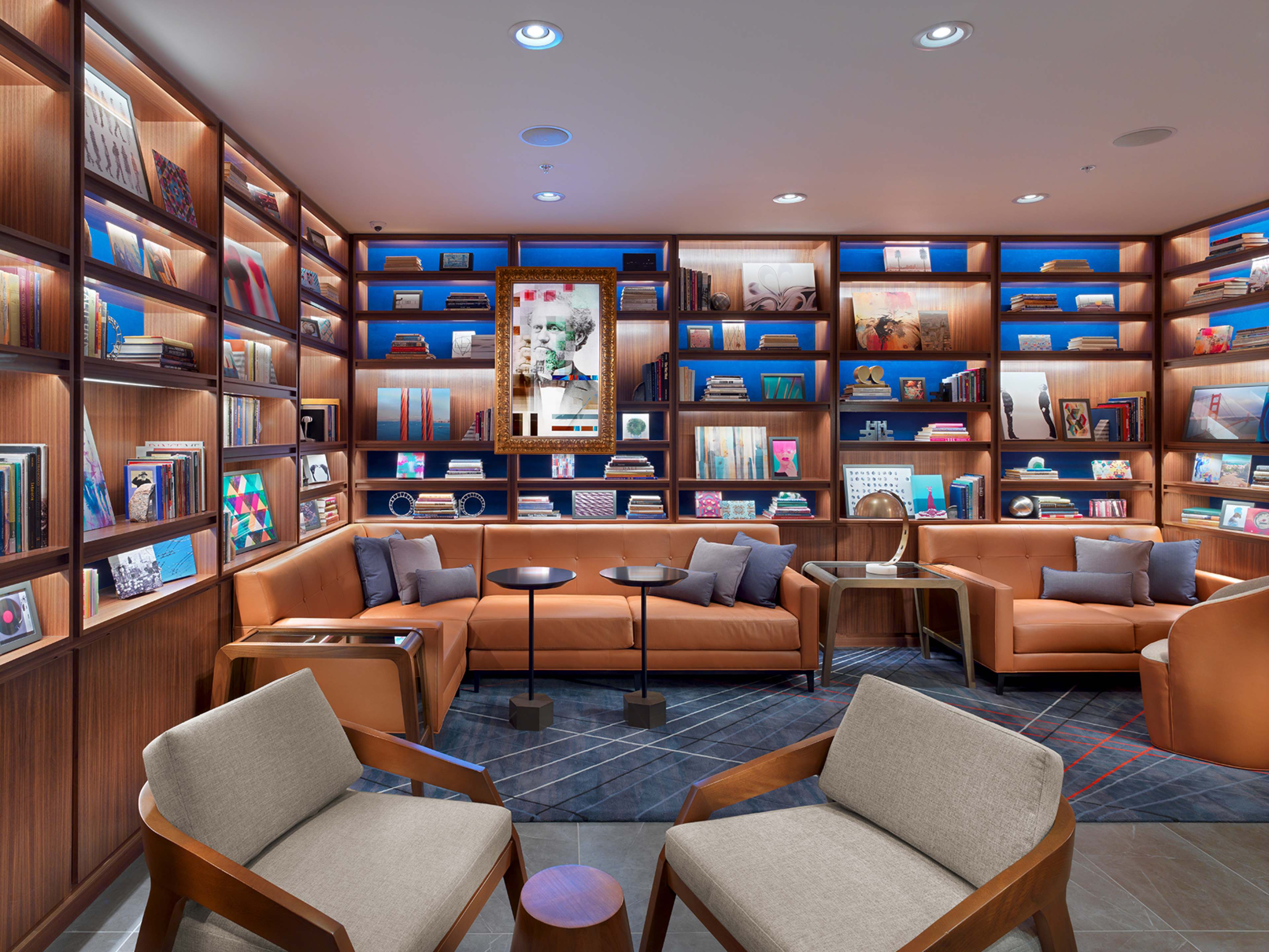 The image depicts a modern lounge area featuring a set of bookshelves filled with various books and decorative items, alongside comfortable seating arrangements.