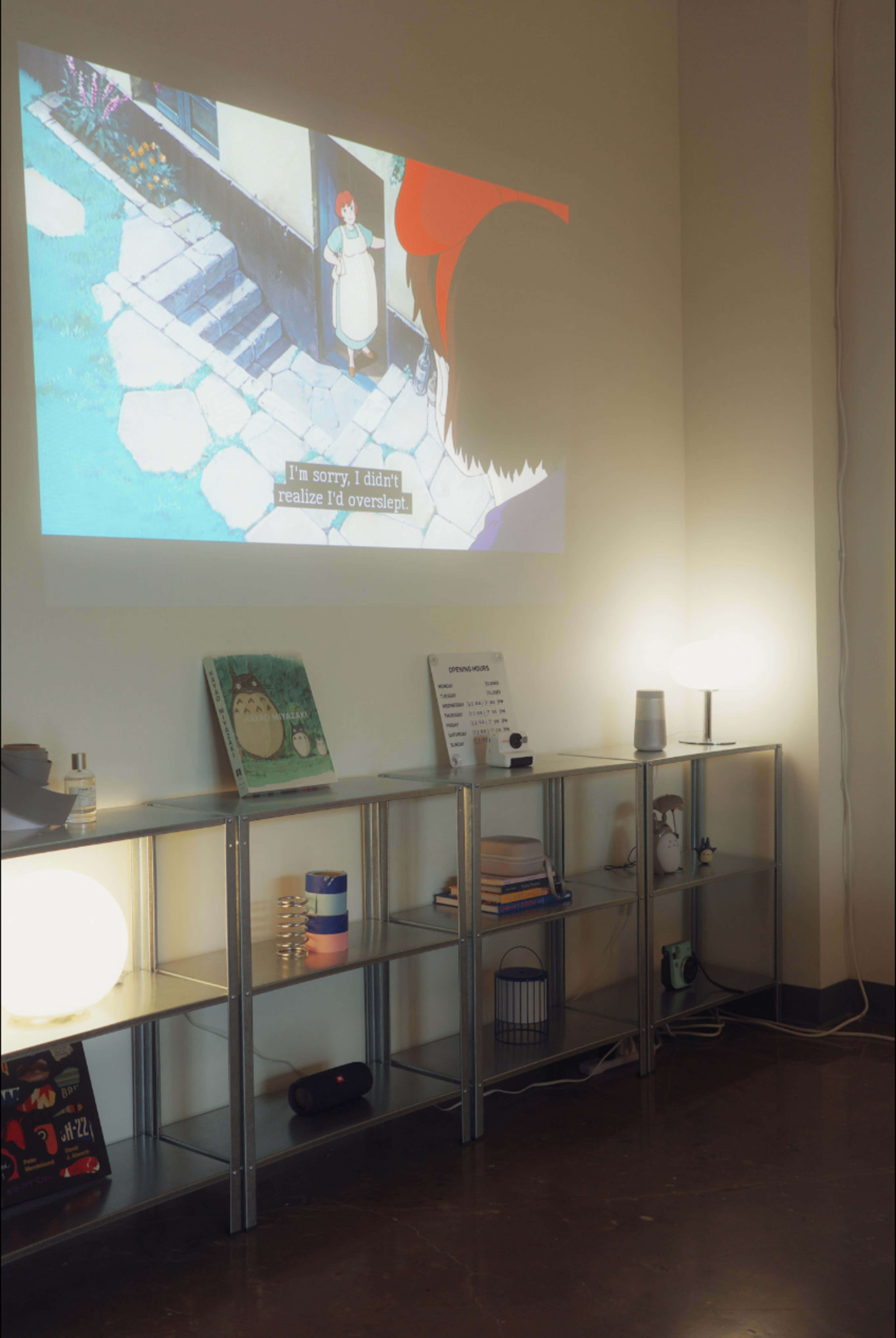 A projector displays an animated scene on a wall while a shelving unit holds various items, including books and decorative objects.