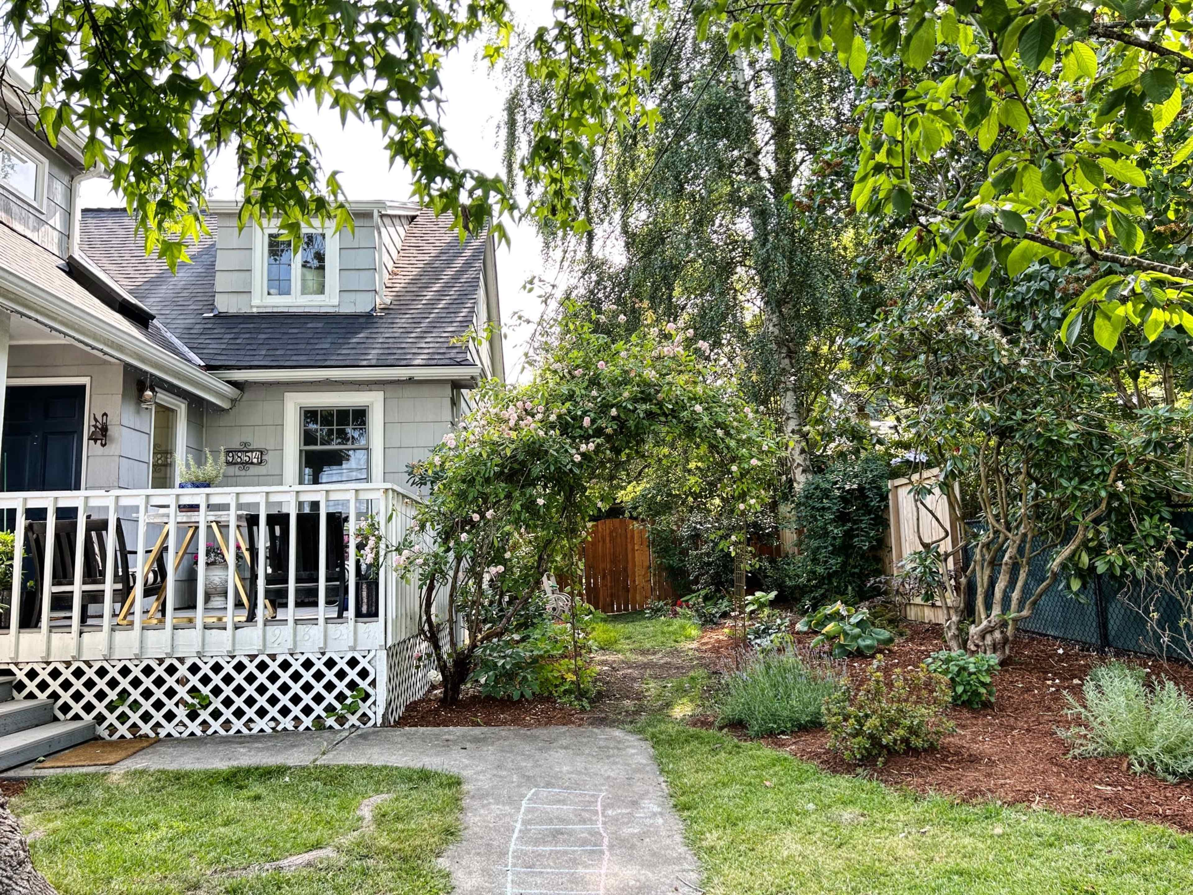A residential property with a wooden porch, a well-maintained garden, and a pathway leading through lush greenery.