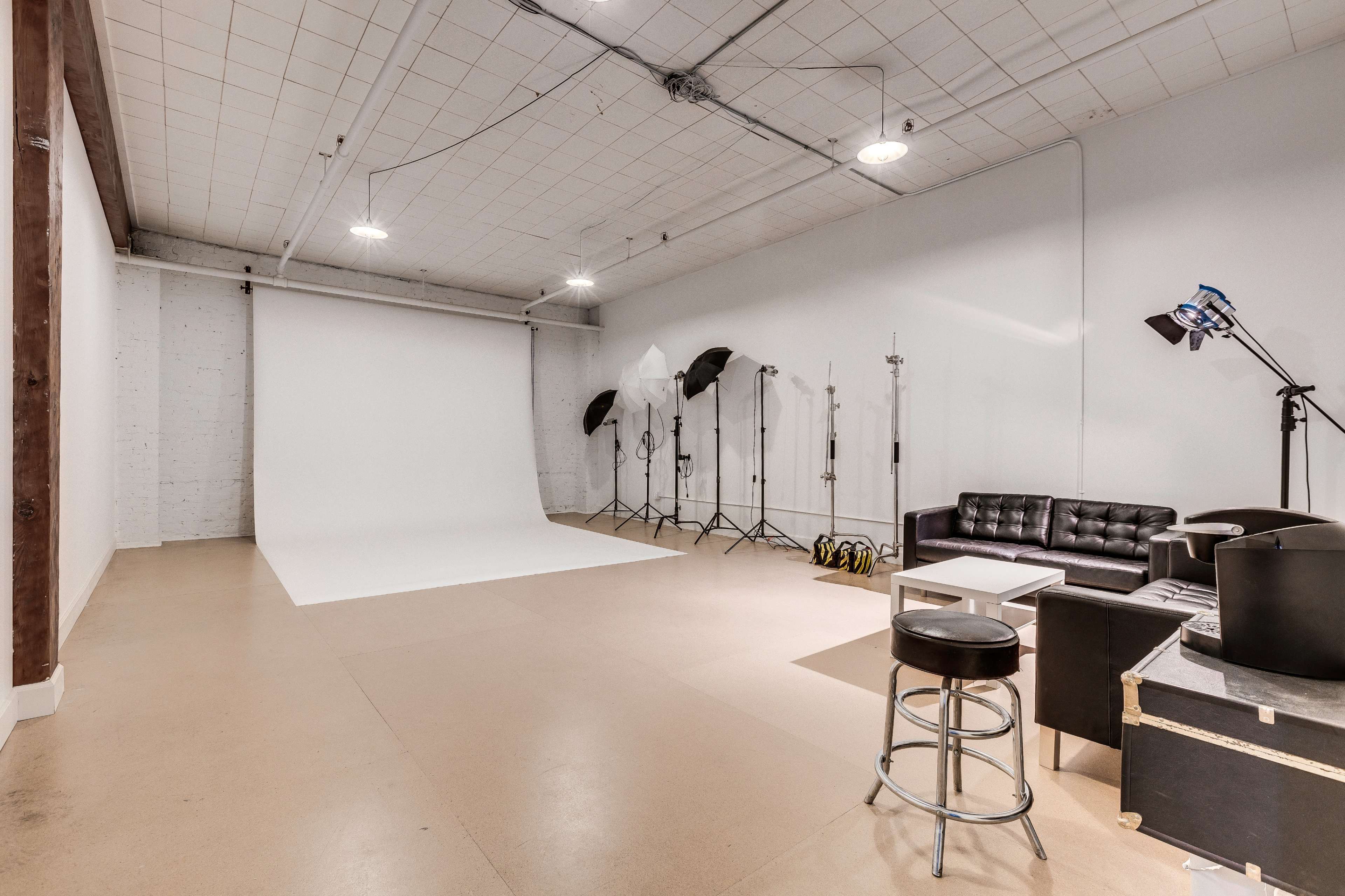 A spacious photography studio with a white backdrop, lighting equipment, and a black couch.