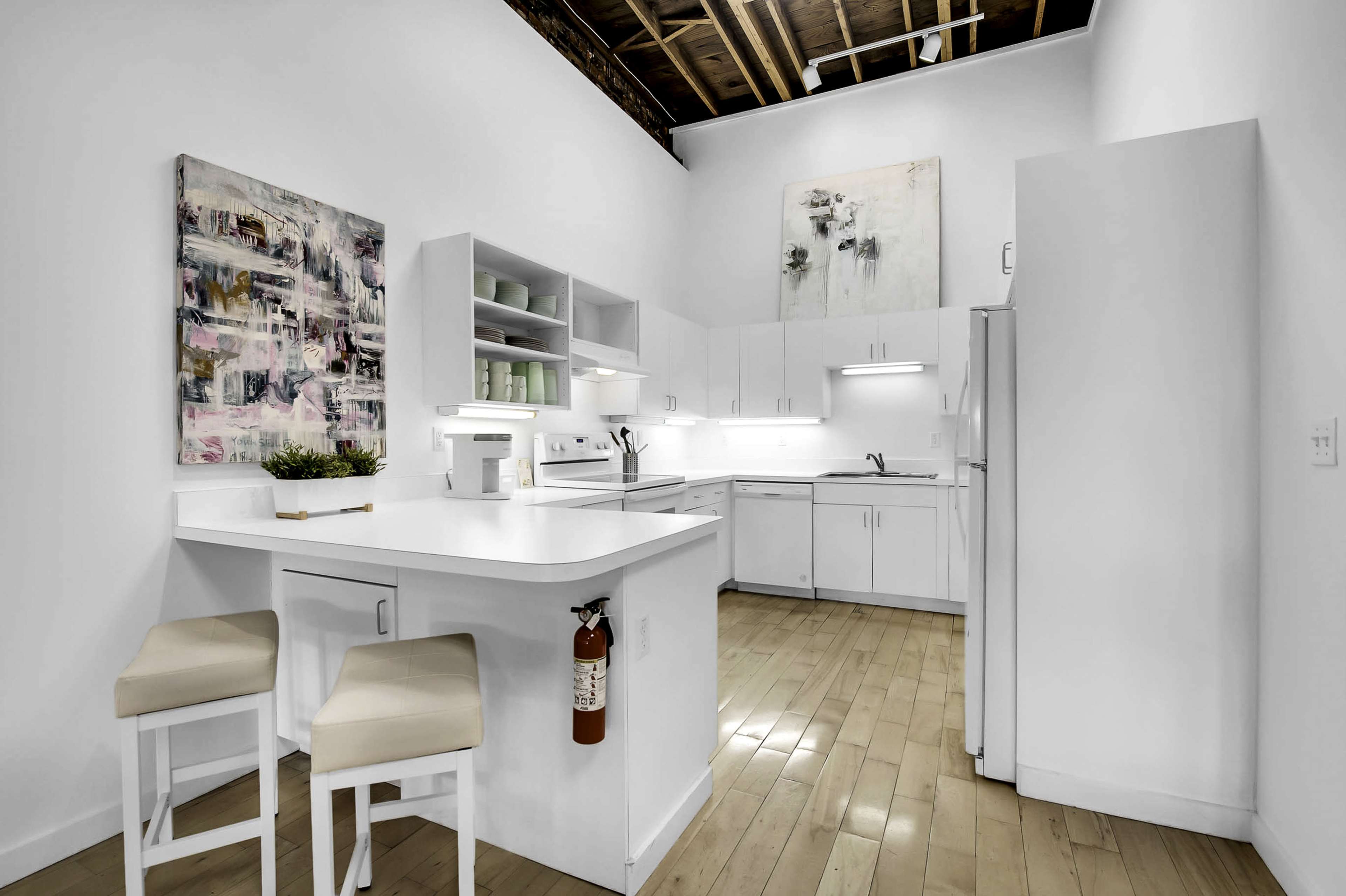 A modern kitchen featuring white cabinetry, a central island with seating, and a mix of artwork on the walls.